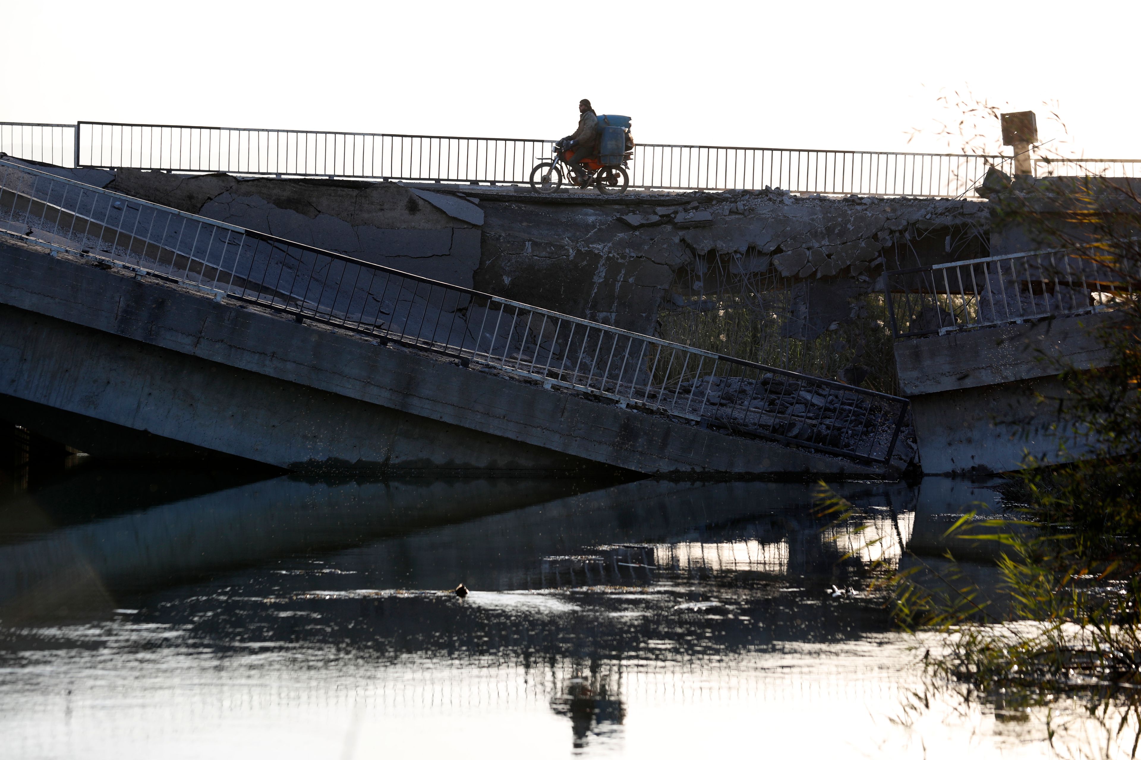 A man on his motorcycle passes by a bridge that links to Lebanon which was destroyed on Oct. 24 by an Israeli airstrike, in Qusair, Syria, Sunday, Oct. 27, 2024. (AP Photo/Omar Sanadiki)