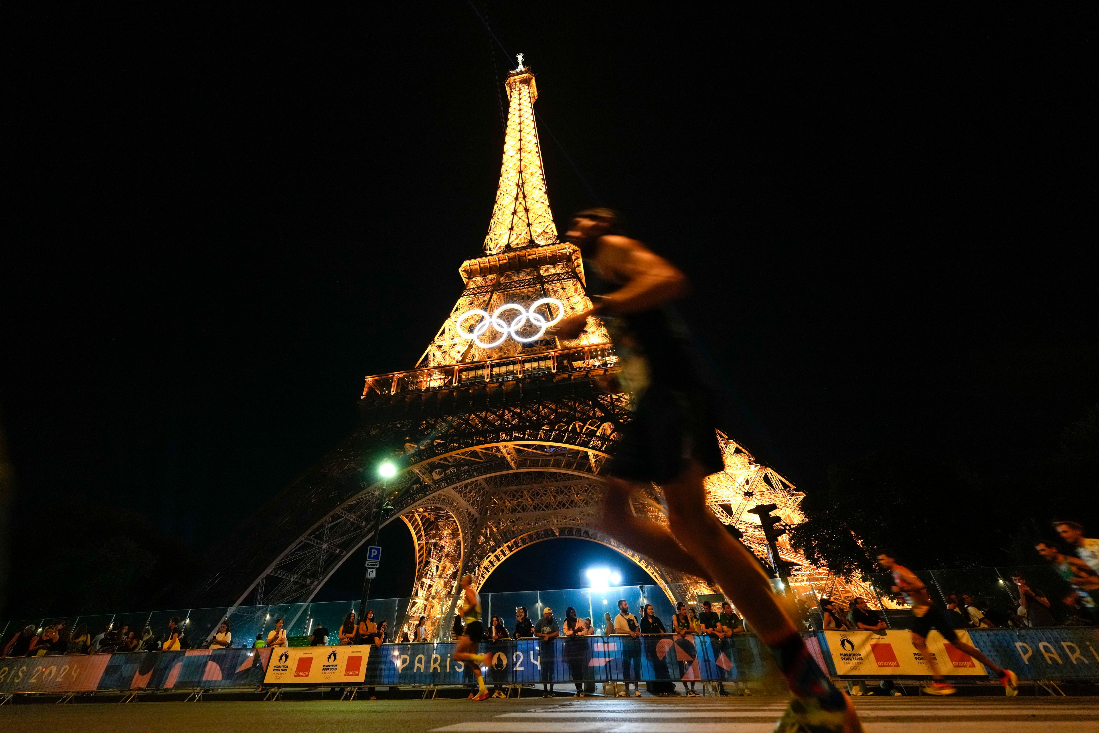 Spectators stand at the base of the Eiffel Tower as they watch runners participate in the Pour Tous marathon, at the 2024 Summer Olympics, in Paris, Saturday, Aug. 10, 2024. (AP Photo/Natacha Pisarenko)