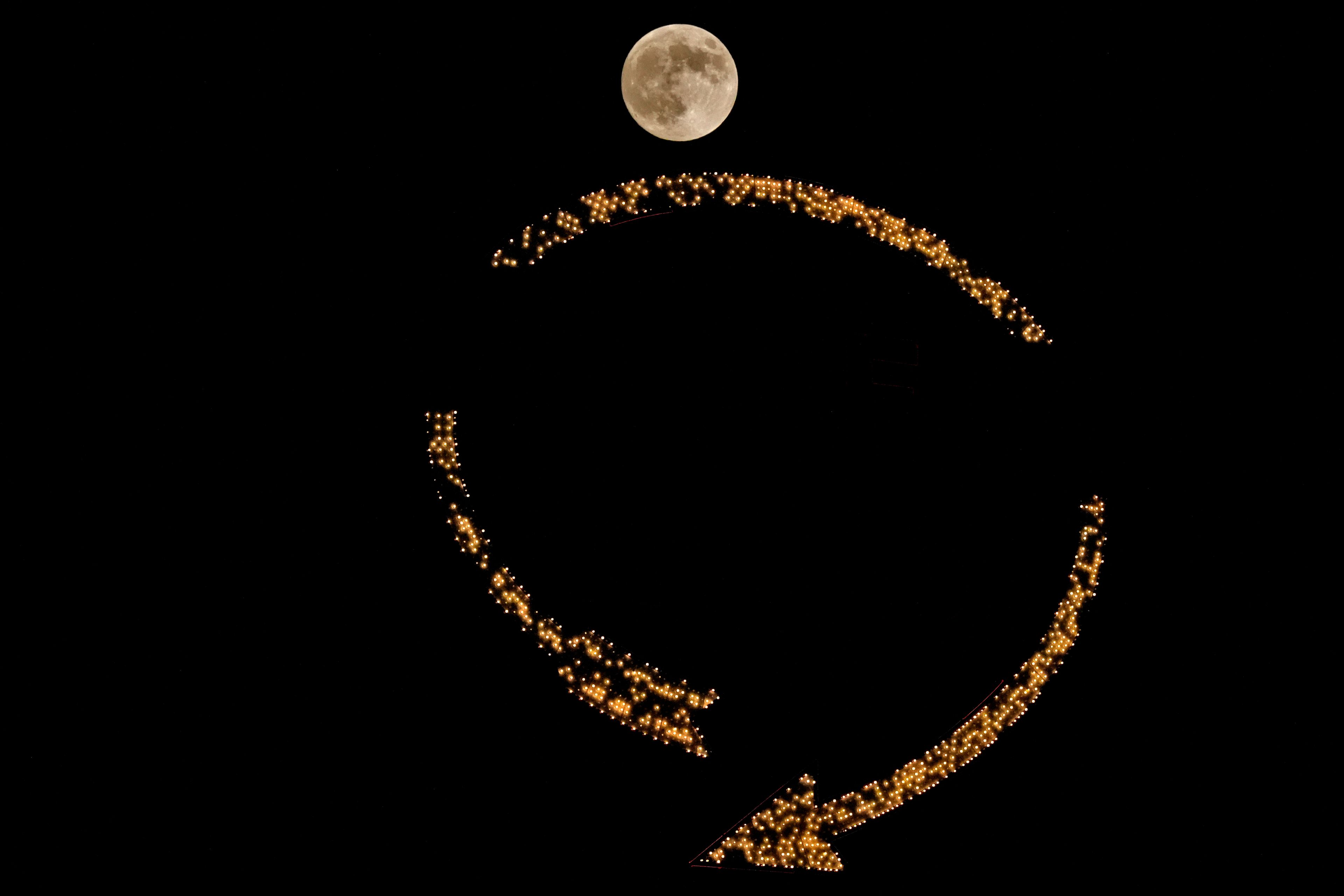 The moon rises beyond an antique sign atop a downtown apartment building, Wednesday, Oct. 16, 2024, in Kansas City, Mo. (AP Photo/Charlie Riedel)