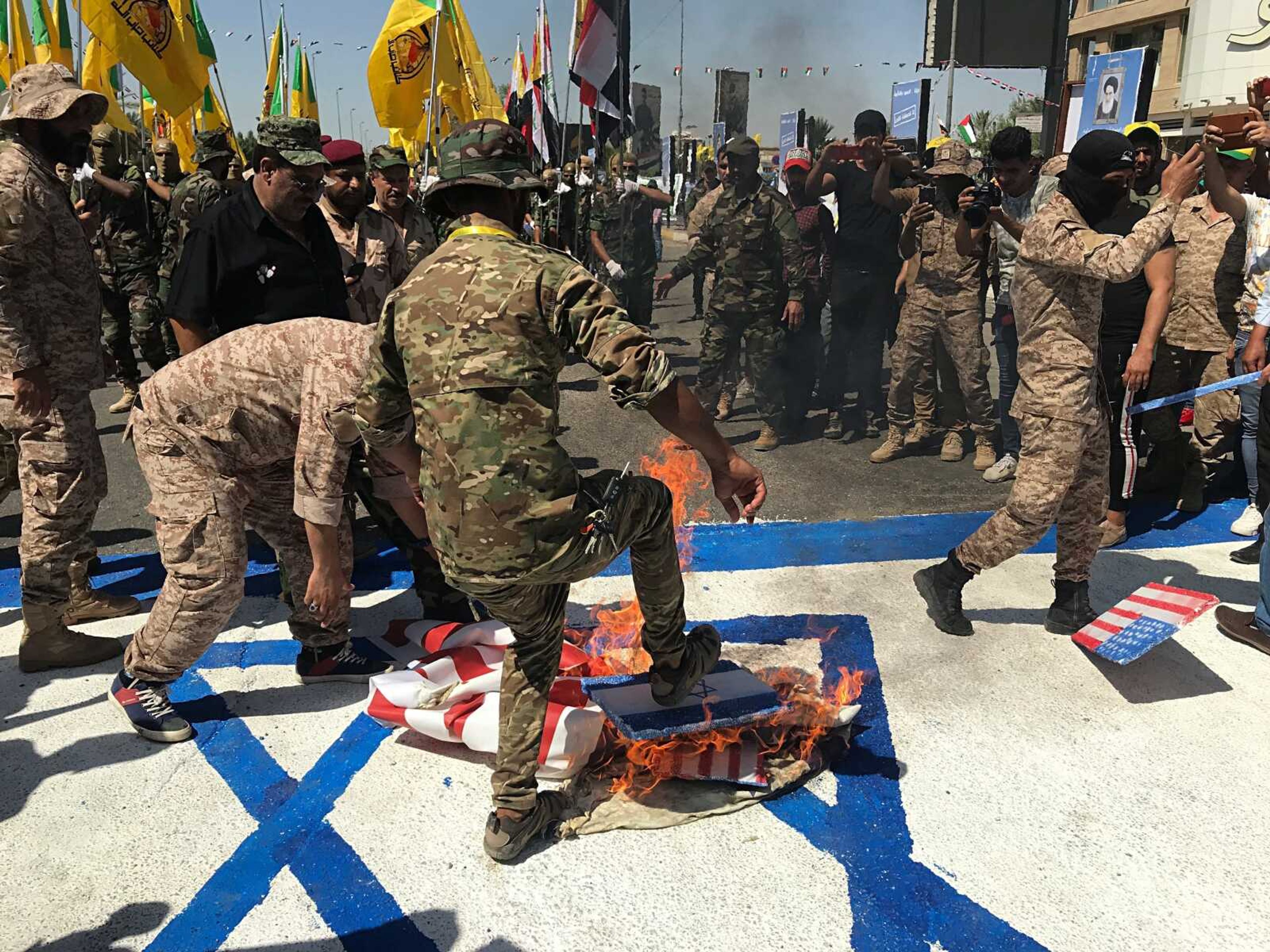 FILE - in this Friday, May 31, 2019 file photo, Iraqi Popular Mobilization Forces burn representations of U.S. and Israeli flags during  al-Quds  Day, Arabic for Jerusalem, in Baghdad, Iraq. Israel was responsible for the bombing of an Iranian weapons depot in Iraq in July, U.S. officials have confirmed, an attack that would mark a significant escalation in Israel's long campaign against Iranian military entrenchment in the region. (AP Photo/Ali Abdul Hassan, File)