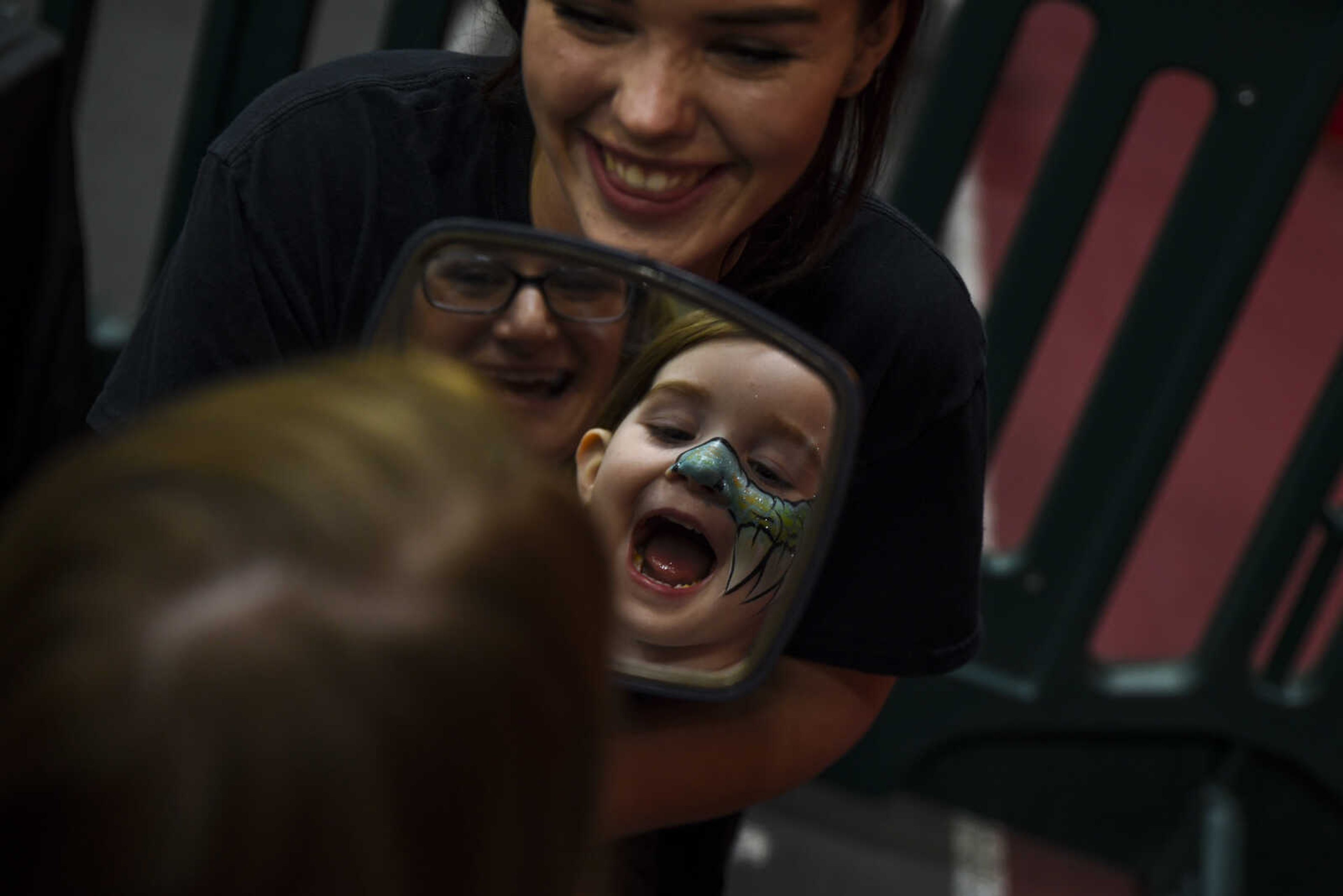 Willa Cisne, 3, held by her mom Alicia Cisne, reacts to her face paint as Hannah Cobb holds up a mirror at Jurassic Quest Friday, April 27, 2018, at the Show Me Center in Cape Girardeau.