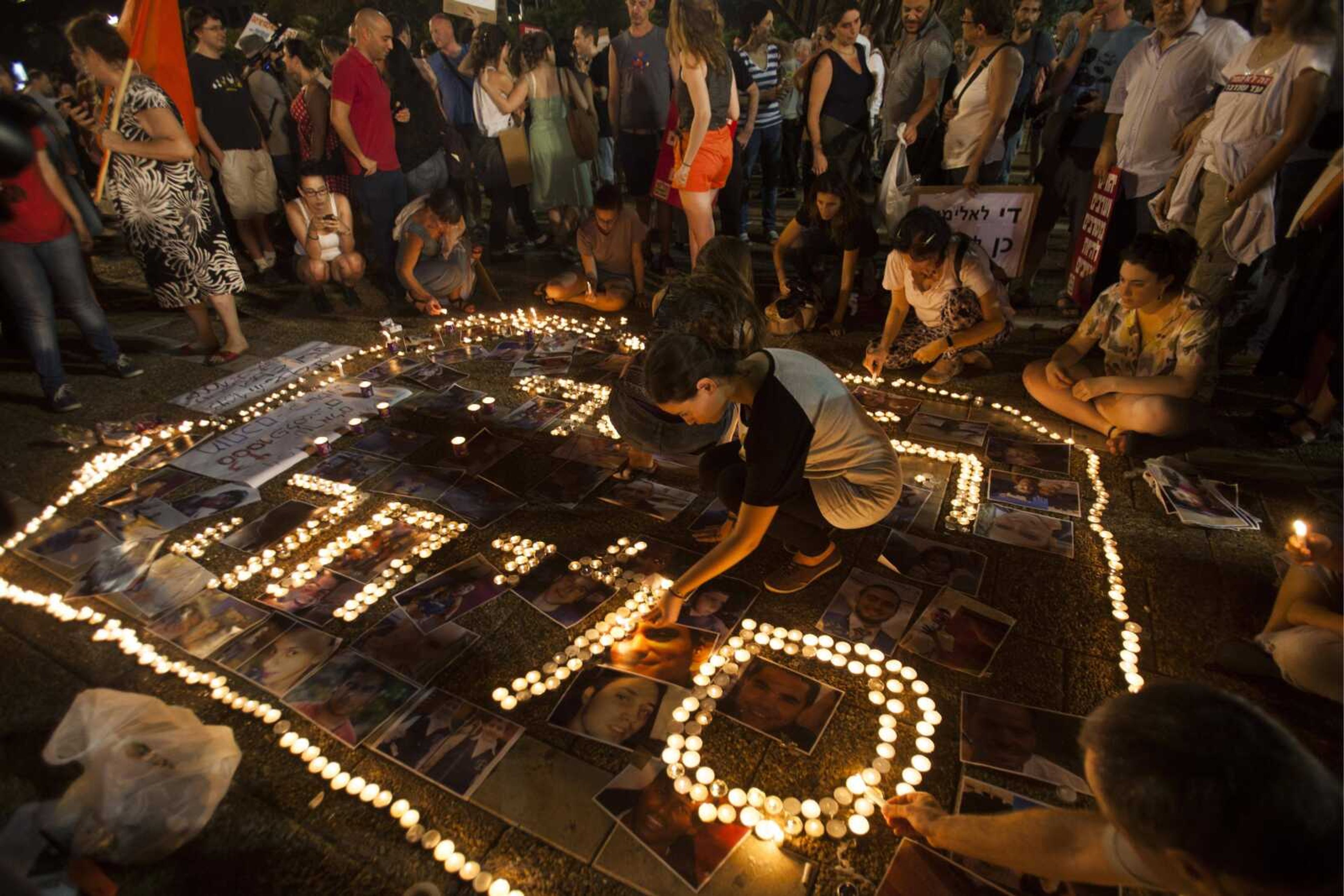 Israeli left-wing activists light candles with shape of the word "Sorry" in Hebrew and place portraits on the ground of Israelis and Palestinians who have been killed in the conflict during a demonstration Saturday against the Gaza war in Tel Aviv, Israel. (Dan Balilty ~ Associated Press)