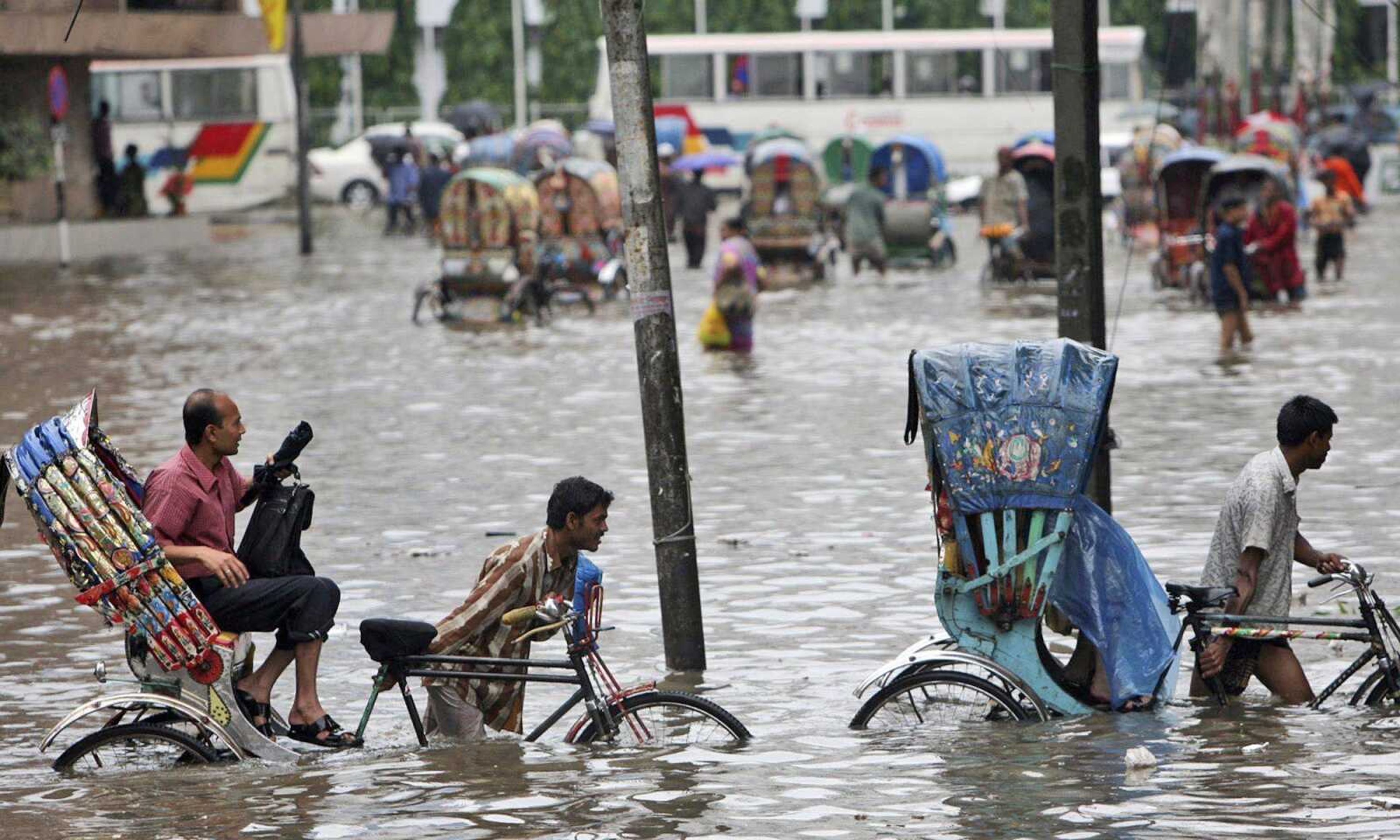 Drivers pull their rickshaws Tuesday through a flooded street in Dhaka, Bangladesh. Heavy monsoon rains have battered Bangladesh&#8217;s capital, flooding streets and homes, stranding thousands and forcing businesses and schools to close. (Pavel Rahman ~ Associated Press)