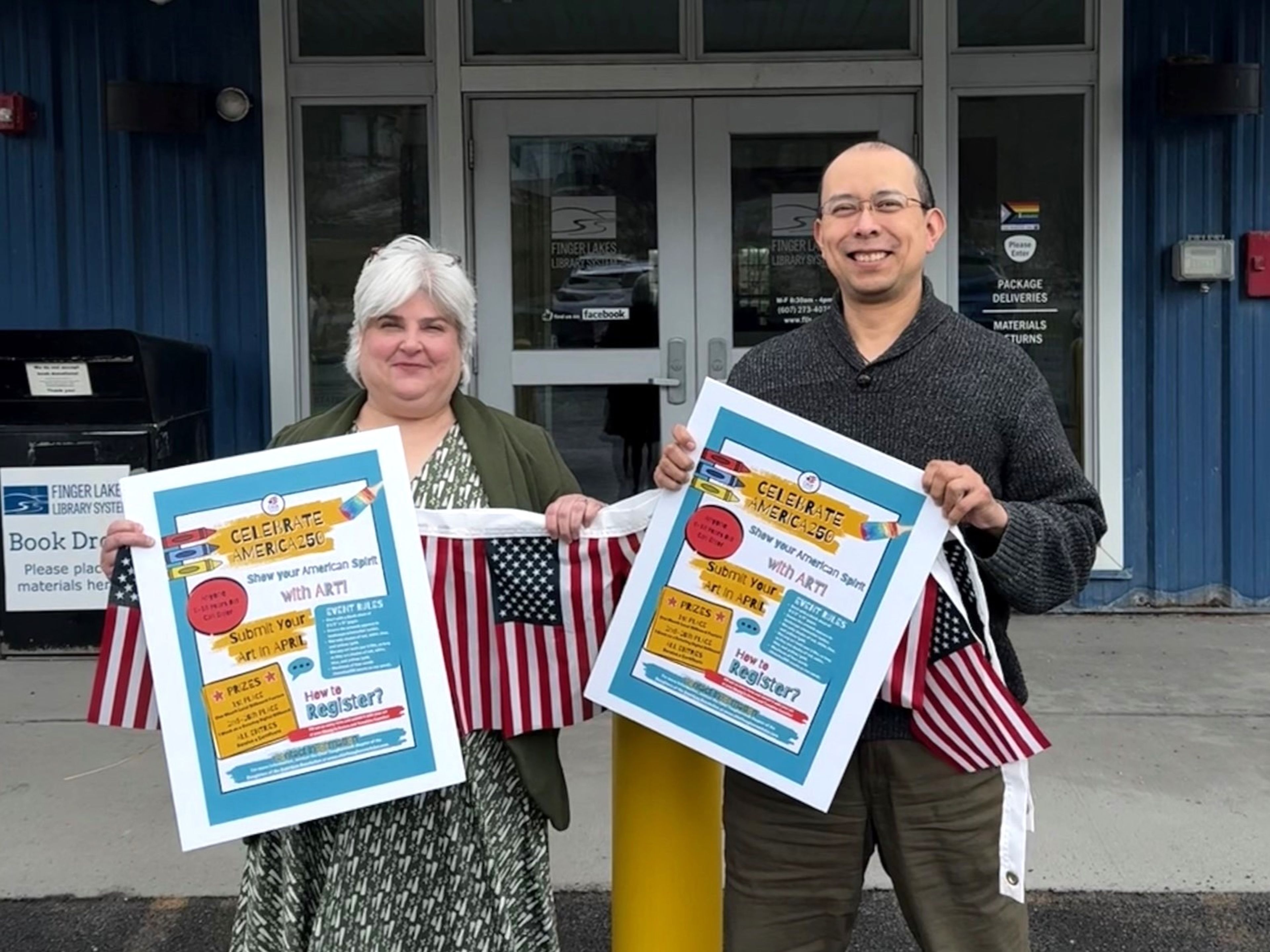 Finger Lakes Library System executive director Sarah Glogowski and business manager Carlos Perez hold promotional posters for the America250 DAR art contest. 
