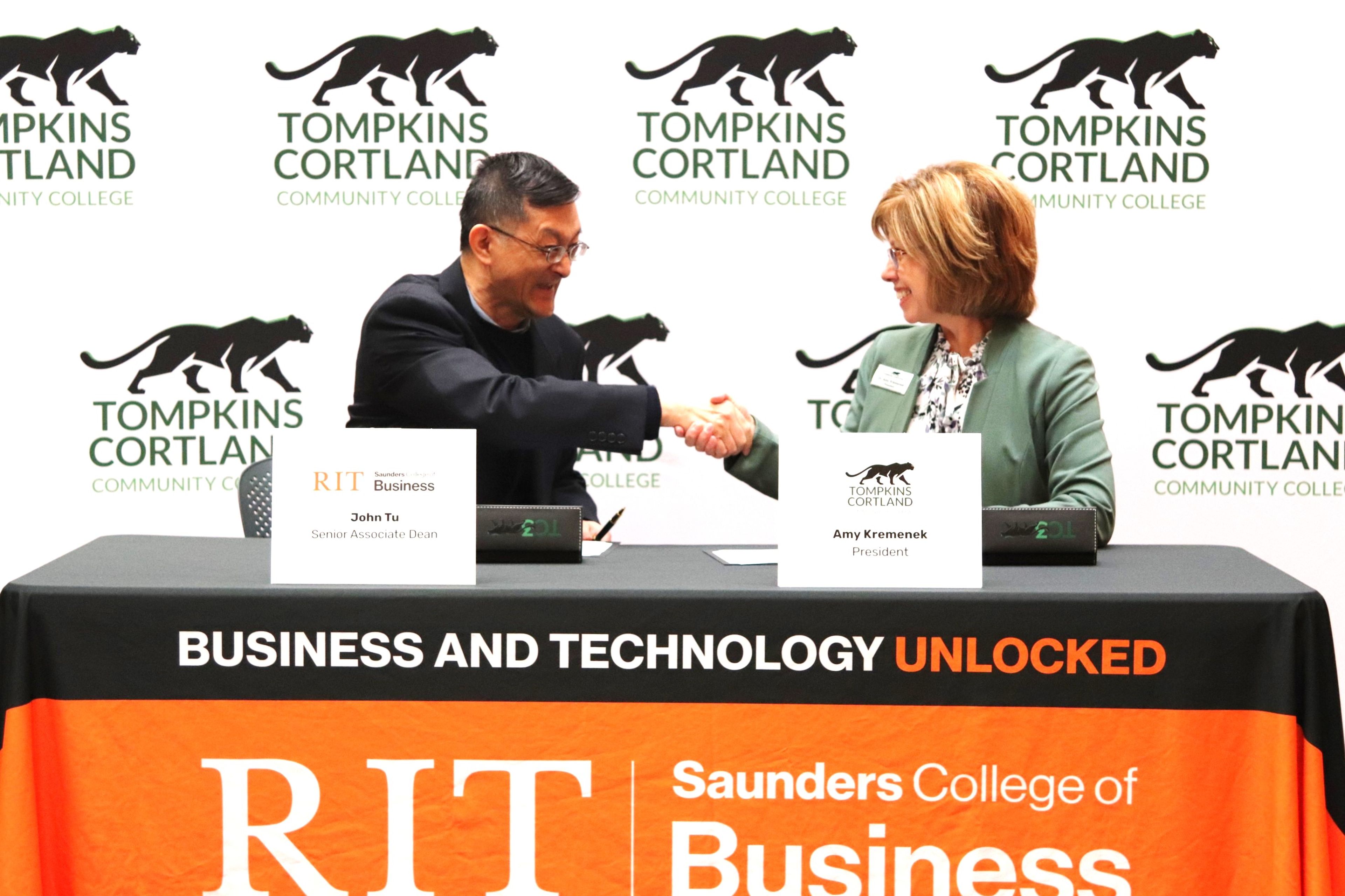 John Tu, RIT's Saunders College of Business senior associate dean, and Amy Kremenek, Tompkins Cortland Community College president, shake hands after reaching three transfer agreements between the colleges.