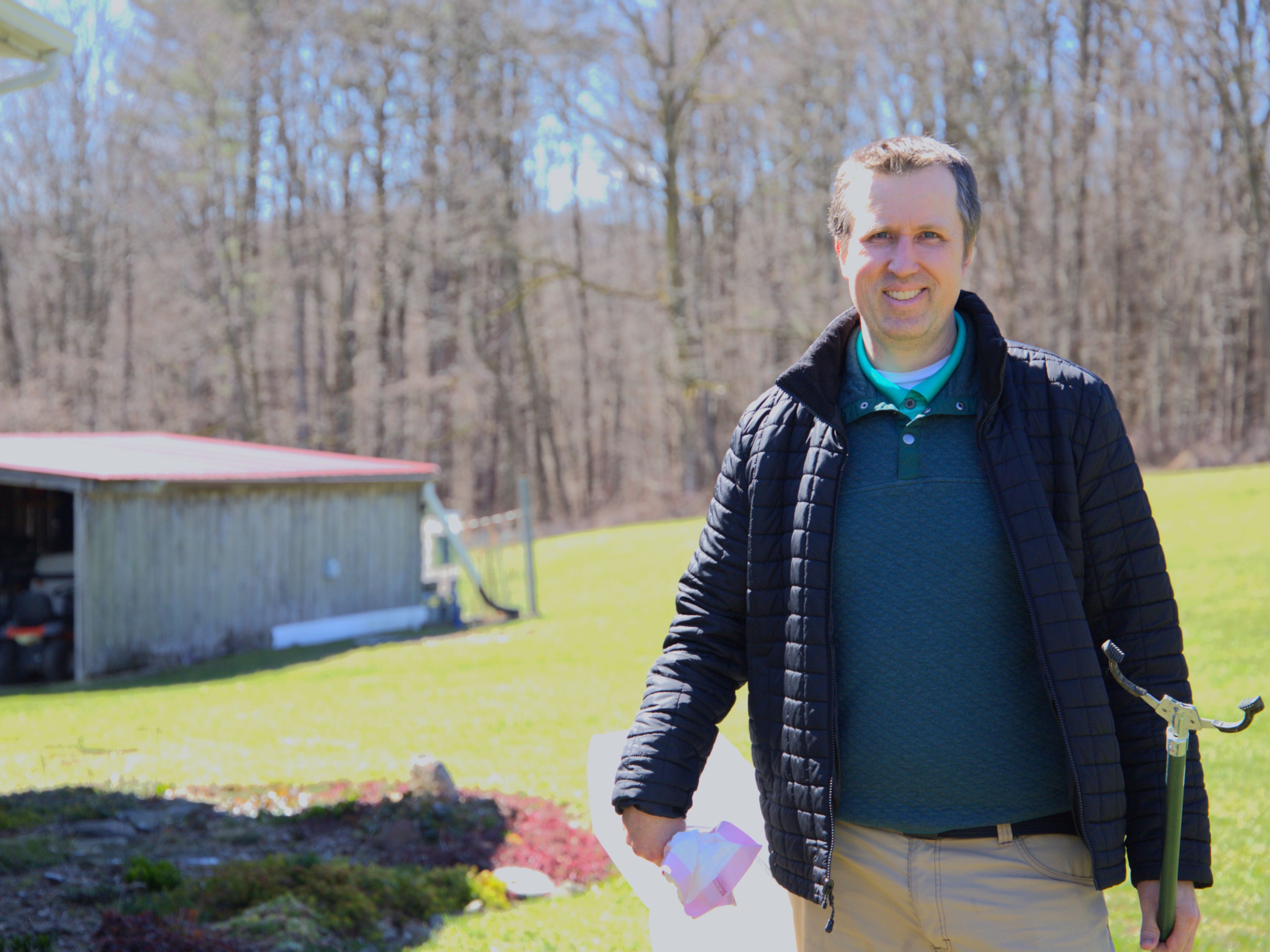 Newfield resident Mitch Raymond stands outside of his home equipped with a garbage bag and a trash grabber. Since 2023, Raymond has organized the annual event Newfield Greenup Day, where community members have helped remove more than 1,000 pounds of trash from the town’s roads every year.  