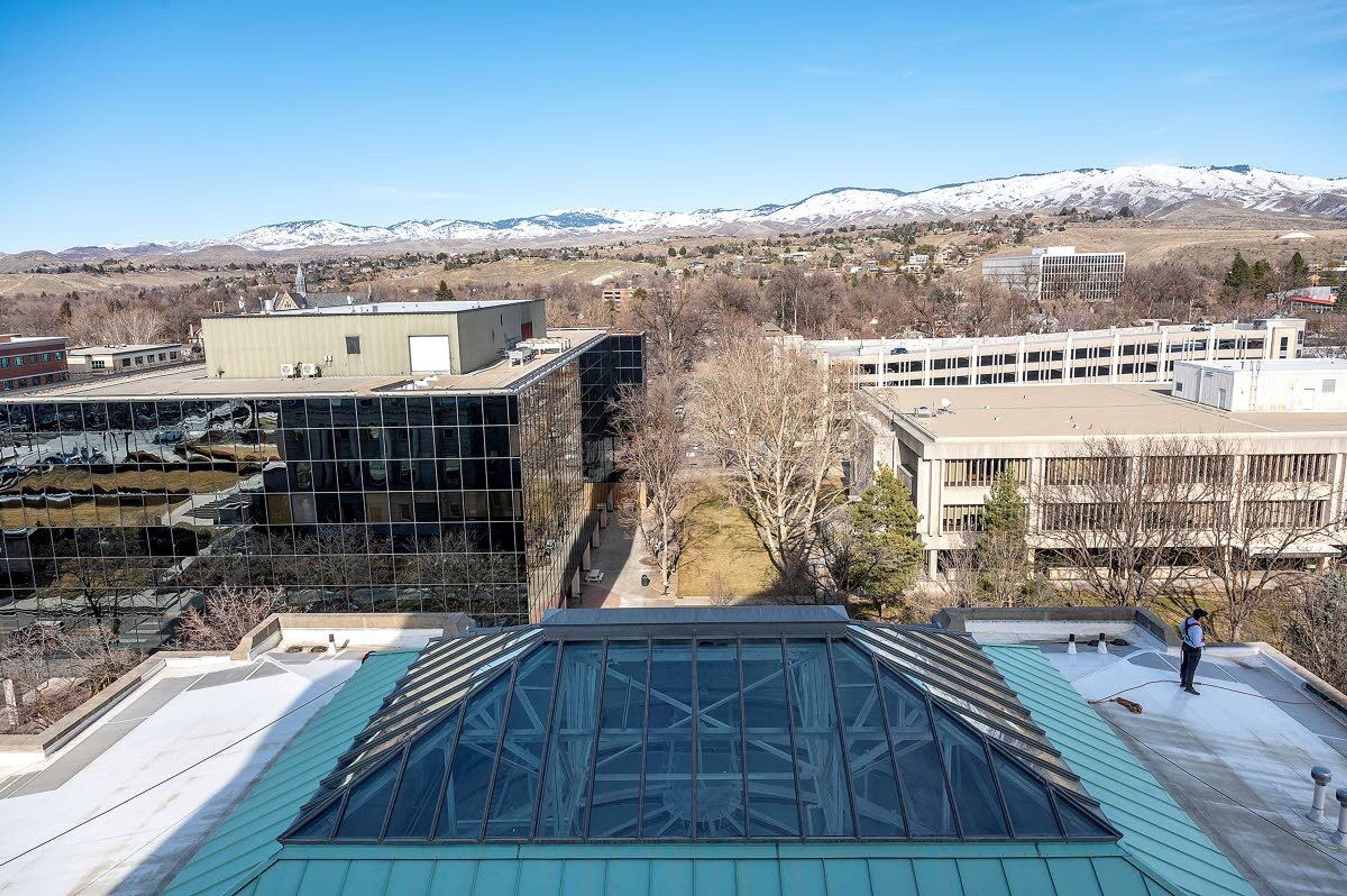 Snowcapped mountains northeast of Boise are seen in the background as a window washer stands above the current home of the Idaho Joint Finance-Appropriations Committee and the former home of the Idaho Supreme Court earlier this month at the Idaho Capitol.