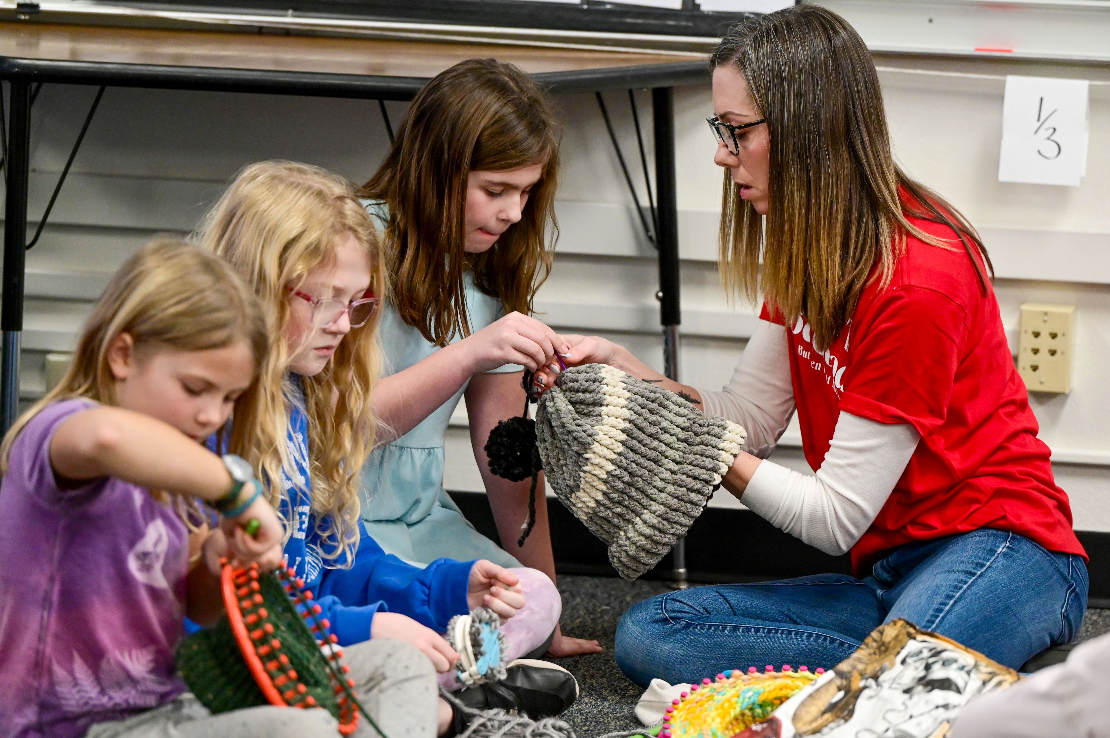 Ayla Delphous, center, a third-grader at Lena Whitmore Elementary School, is helped by fourth-grade teacher Lindsey Lee, right, to secure a pom pom on a hat at the school in Moscow on Monday.