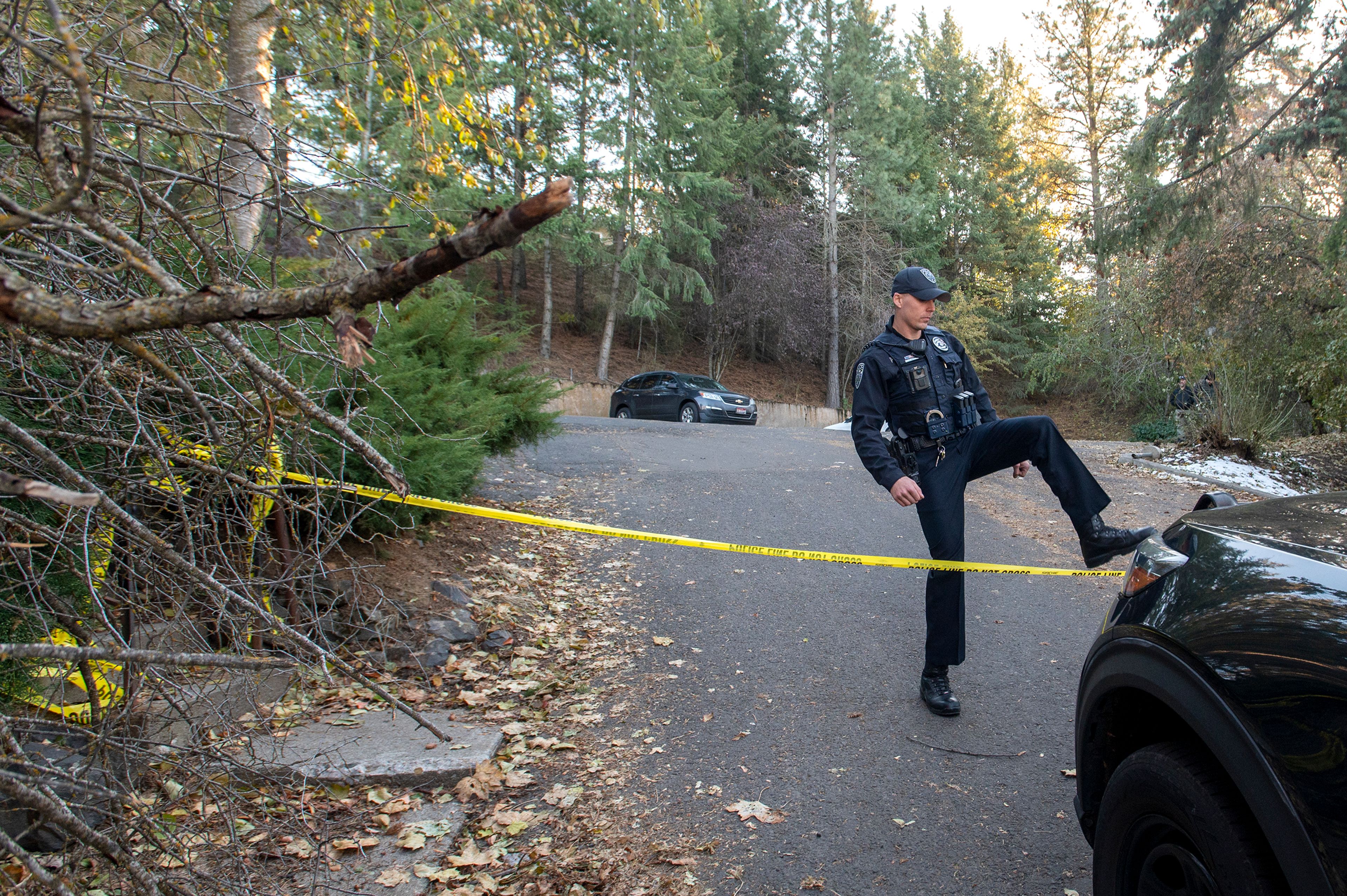 An officer steps over caution tape Monday in a parking lot behind the home where four University of Idaho students were stabbed in a quadruple homicide on King Road in Moscow.