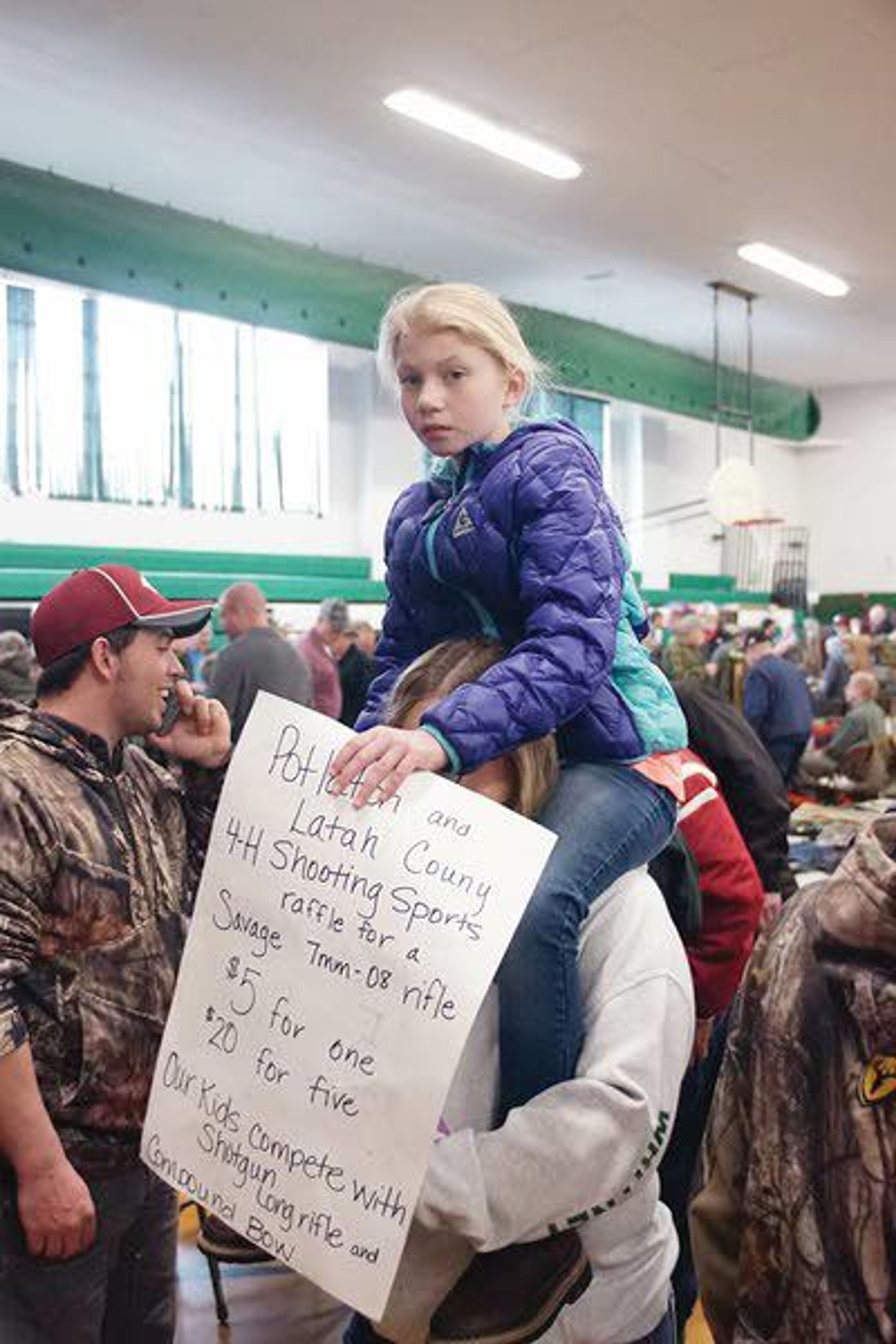 Sophia Lusby rides on Mikayla Whitney’s shoulders while selling raffle tickets for a rifle at the Potlatch Gun Show Sunday morning.