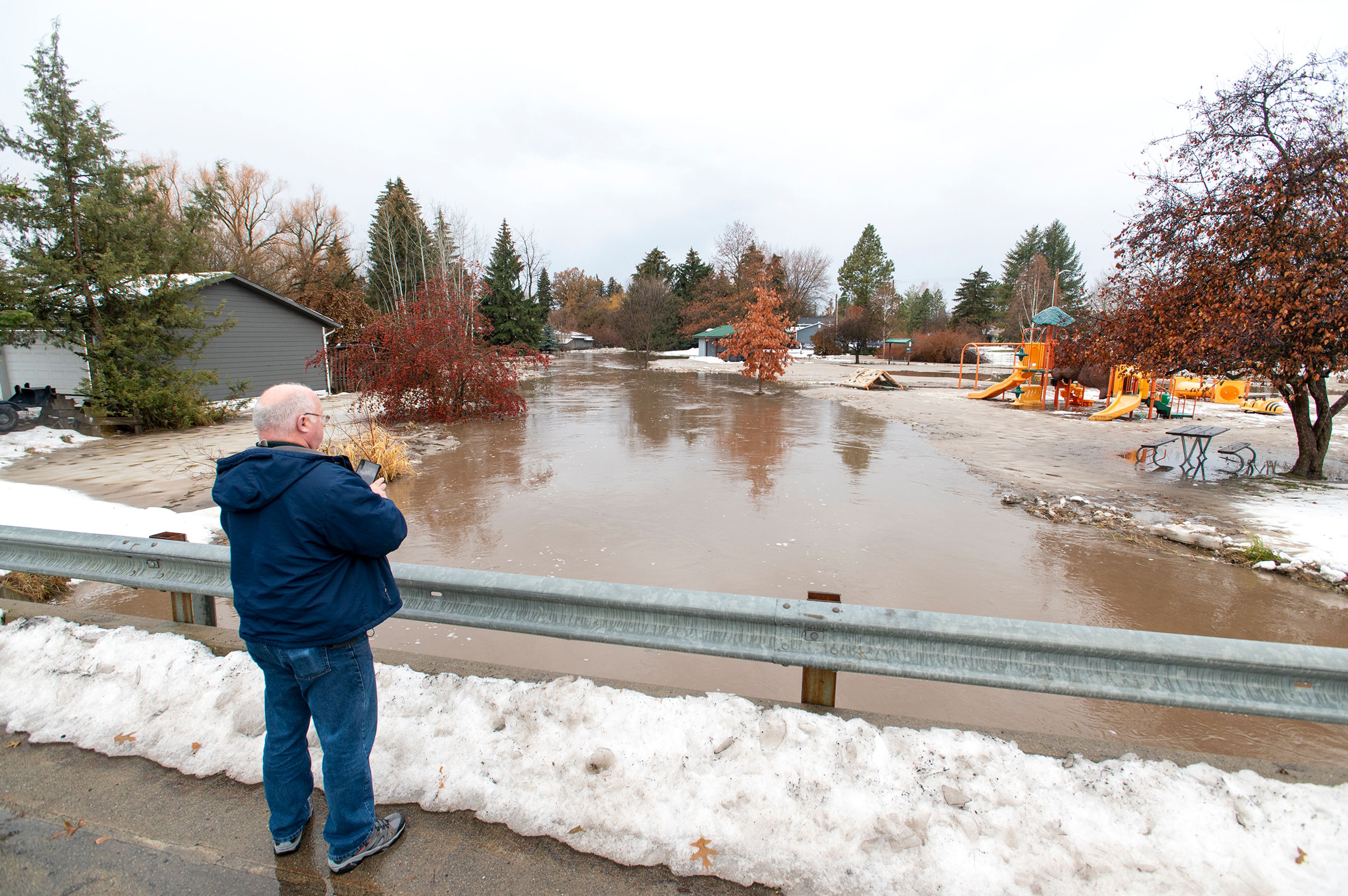 Mike Neelon, the Latah County Disaster Service coordinator, takes pictures on his cell phone of Paradise Creek flooding a playground at Hordemann Pond in Moscow on Tuesday.