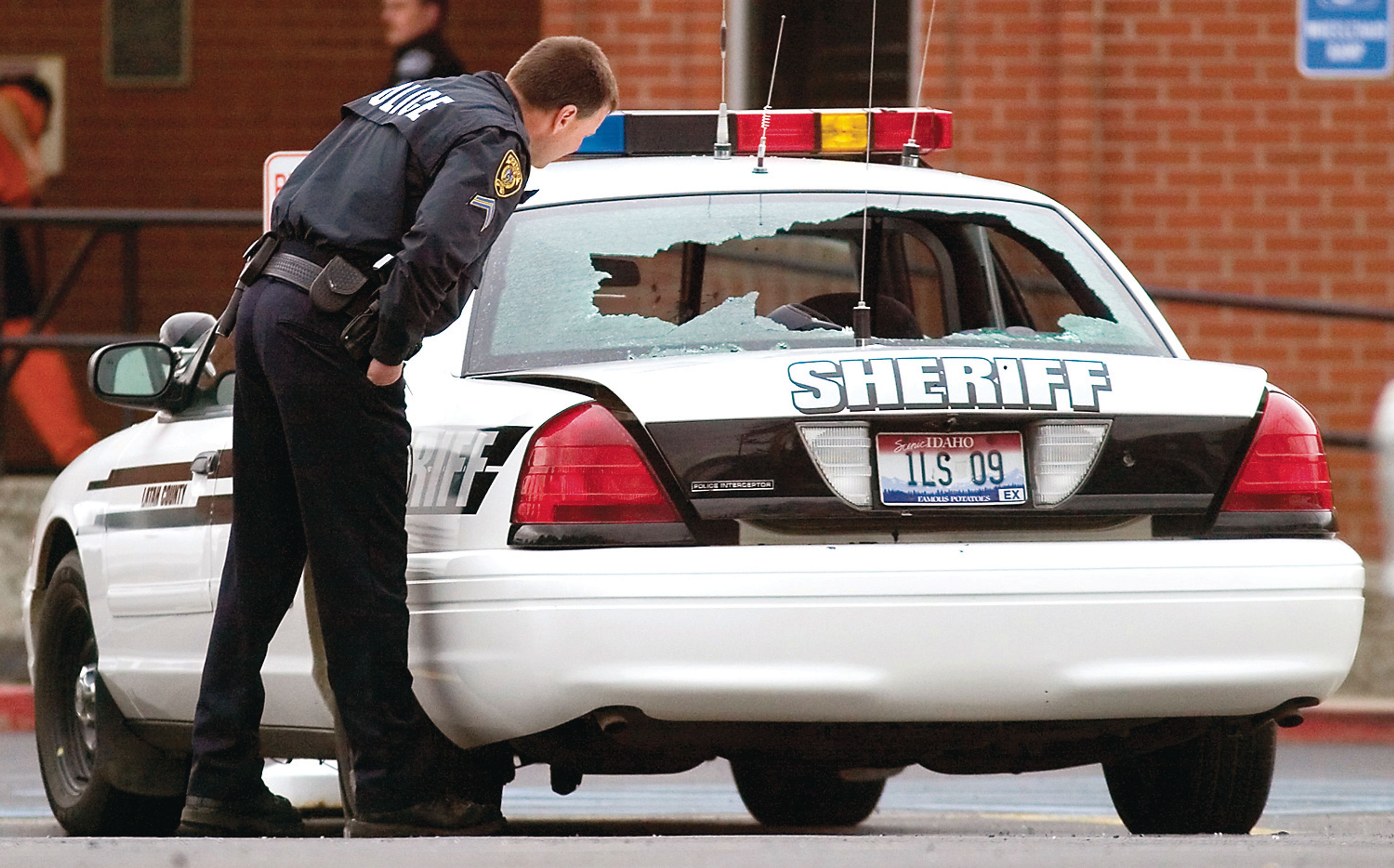 A Moscow police officer looks at the damage to a Latah County Sheriff's Office patrol car outside the courthouse on Monday. Jason Hamilton shot and severely damaged five patrol vehicles and several private vehicles in the courthouse parking lot.