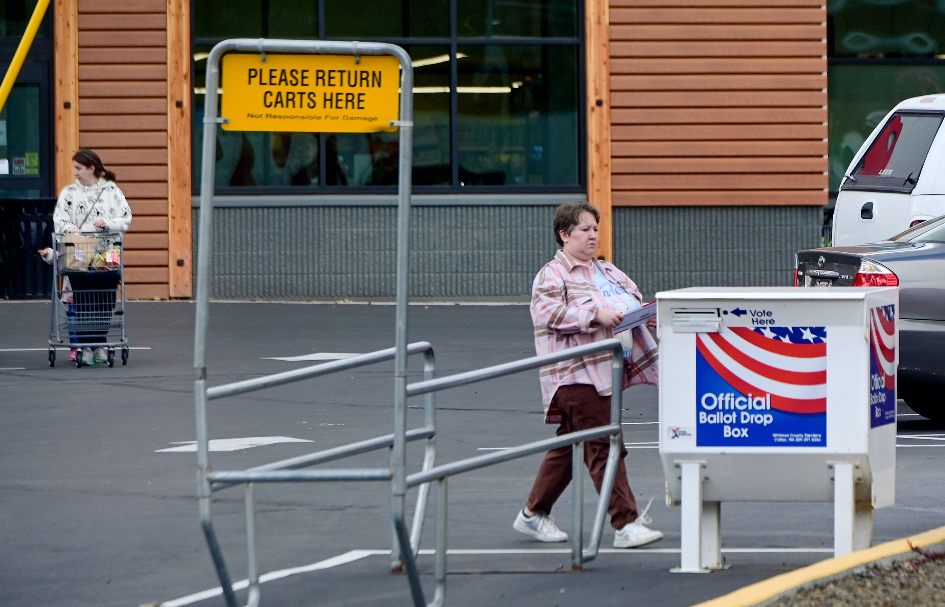 A voter carries their ballot to the drop box located in the parking lot of Rosauers as shoppers exit the grocery store Tuesday in Pullman.