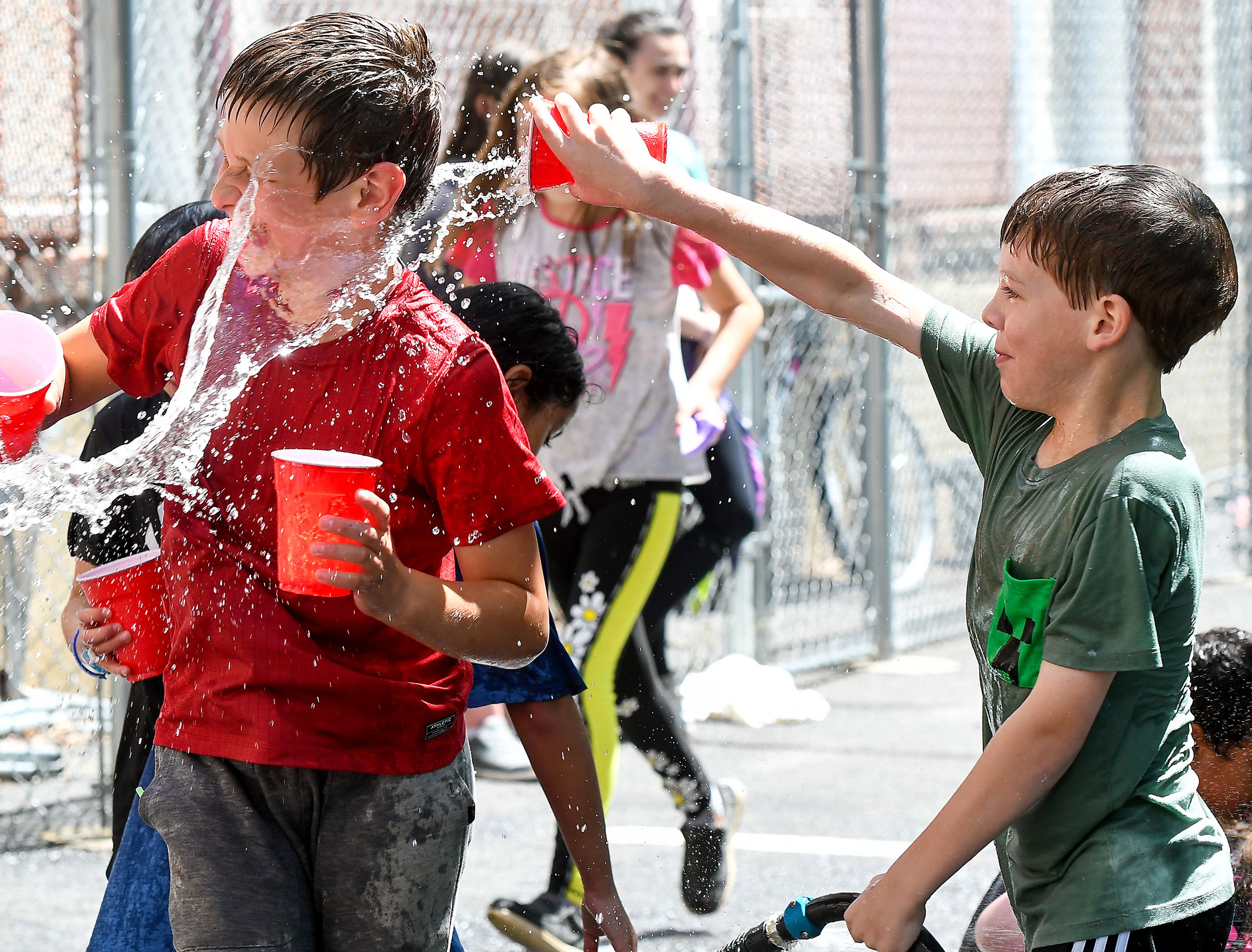 Caden Bieker, left, is doused by Daxton Bailey as students play with water as part of the end of the school year celebration on Russell Elementary’s playground on Wednesday.