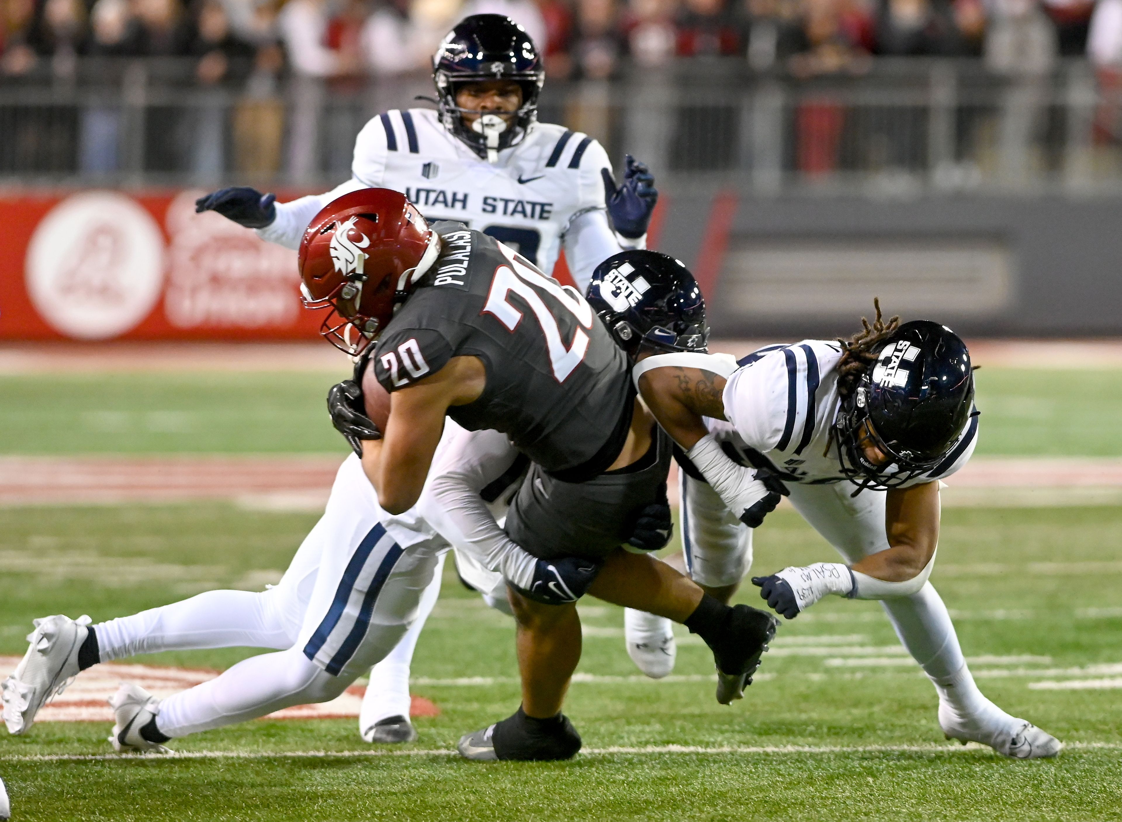 Washington State running back Leo Pulalasi (20) is tackled by Utah State defenders Saturday at Gesa Field in Pullman.