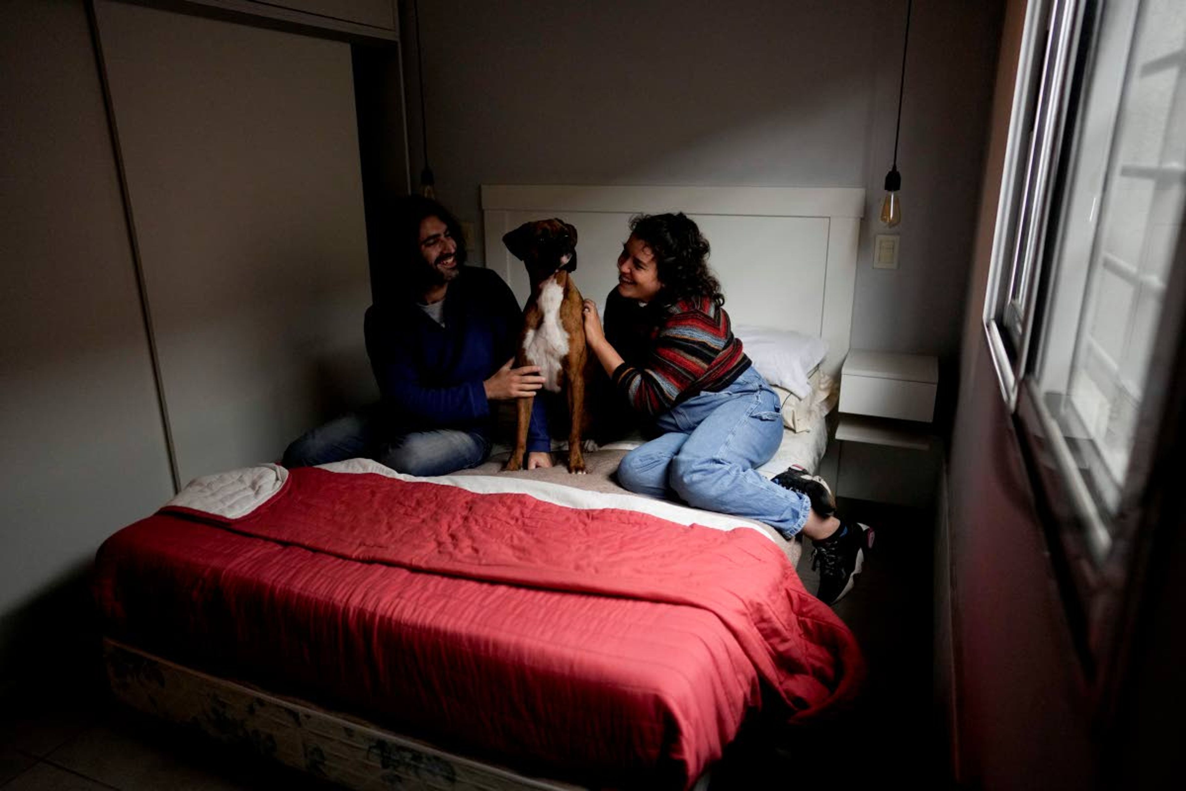 Agustina Ancales and her partner Pablo Vazquez pose for a photo with their dog Sigmoide in Lomas de Zamora, Argentina, Wednesday, Sept. 8, 2021. Ancales' mother got the dog for the couple as a gift after Vazquez was diagnosed with cancer during the COVID-19 lockdown to try to cheer them up. (AP Photo/Natacha Pisarenko)