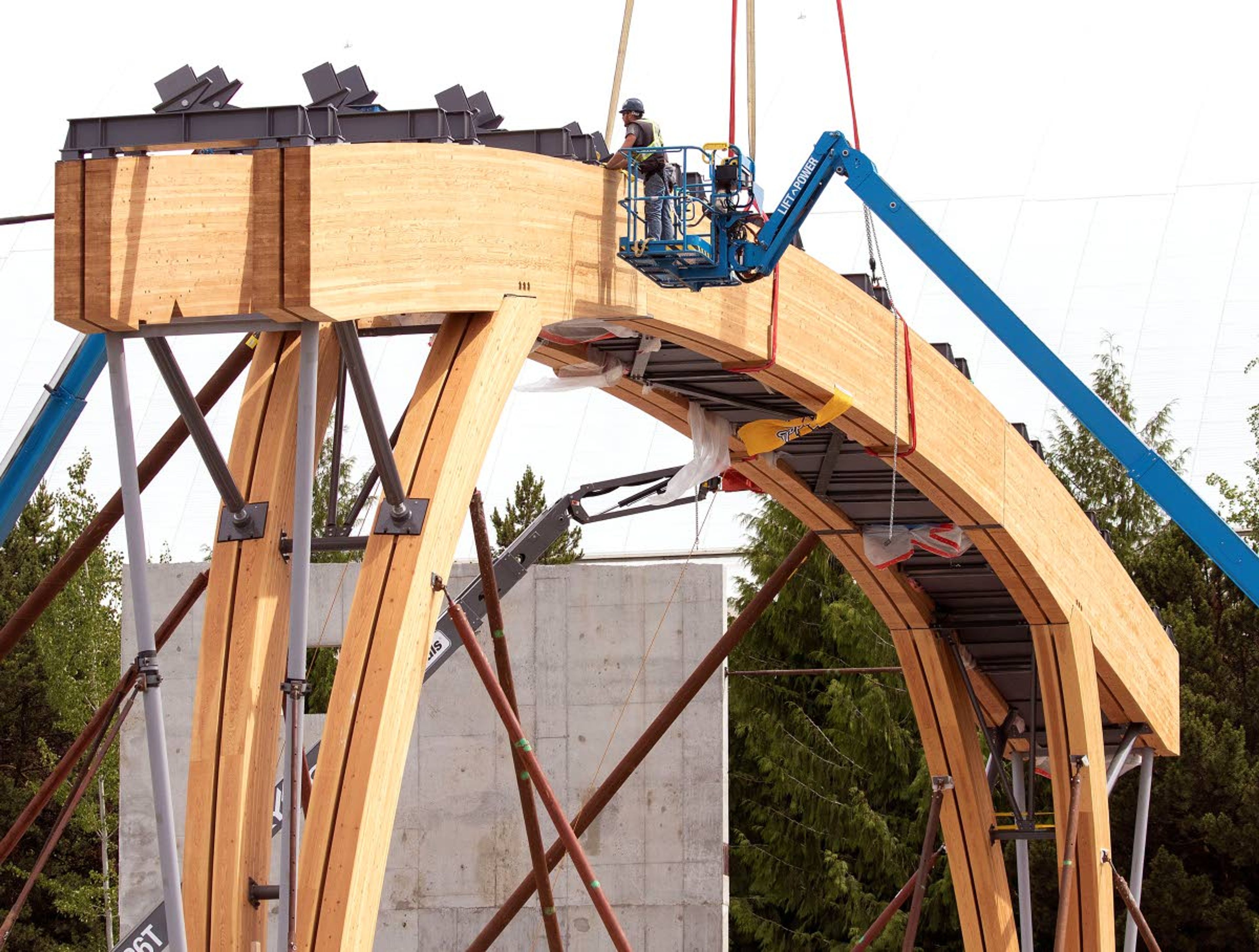 A worker helps secure a laminated wood beam after it was lifted into place with a crane.