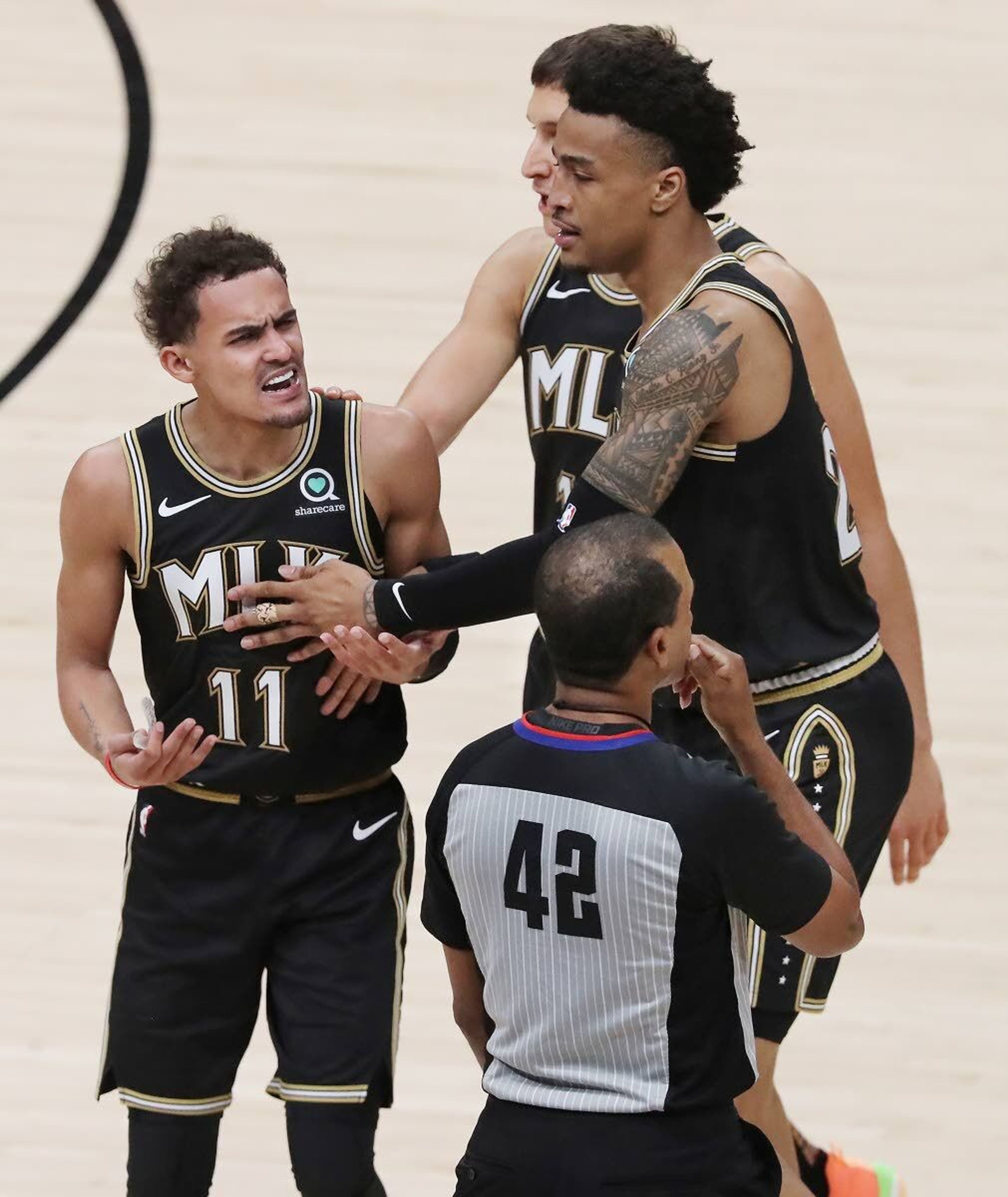 Atlanta Hawks guard Trae Young (11) reacts to being called for a technical foul while John Collins and Bogdan Bogdanovic hold him back from the official during the second quarter in Game 6 of the Eastern Conference finals in the NBA basketball playoffs against the Milwaukee Bucks, Saturday, July 3, 2021, in Atlanta. (Curtis Compton/Atlanta Journal-Constitution via AP)