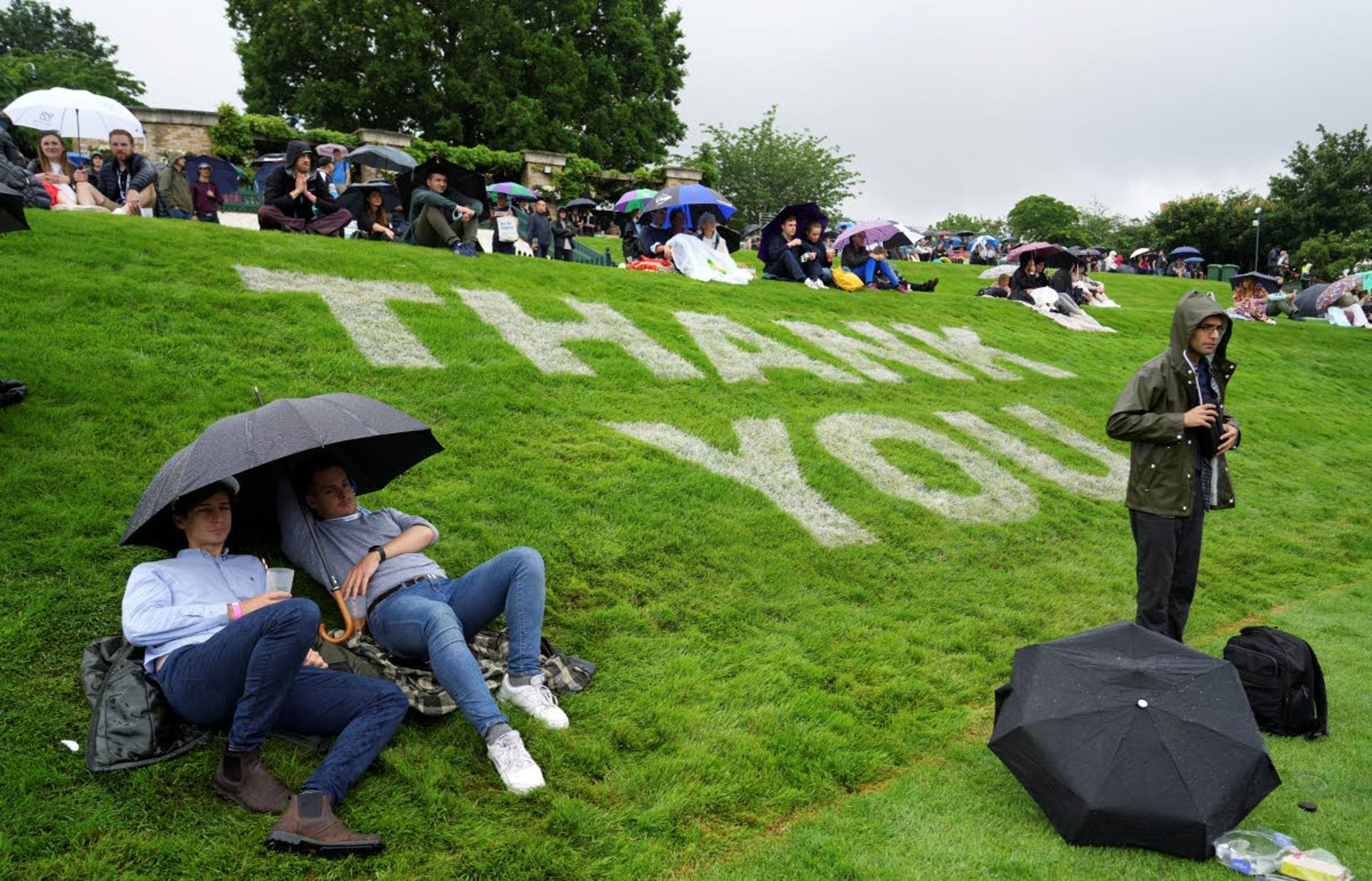 Spectators shelter under umbrellas during a rain delay on day one of the Wimbledon Tennis Championships in London, Monday June 28, 2021. (AP Photo/Alberto Pezzali)