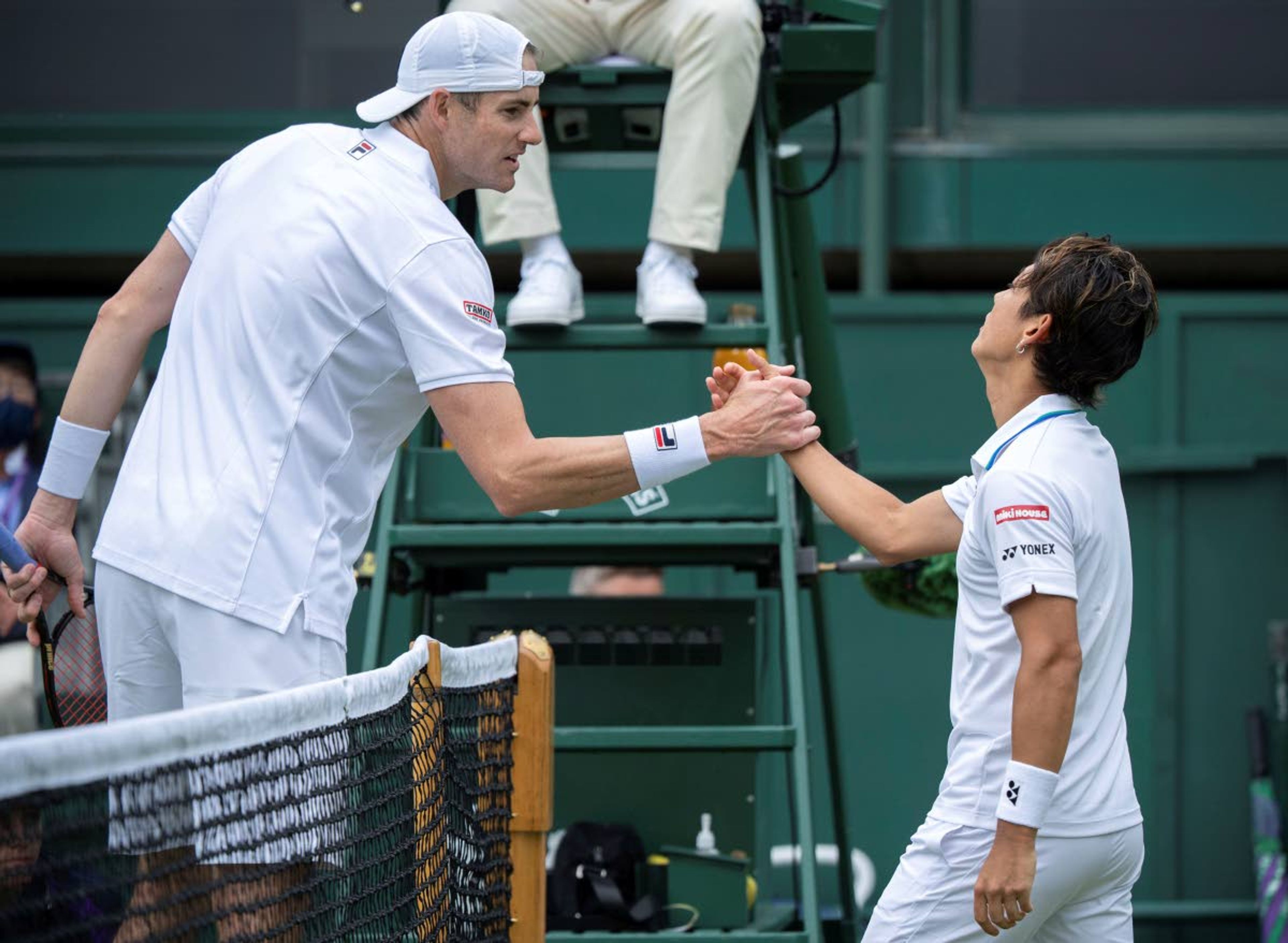 Japan's Yoshihito Nishioka shakes hands with John Isner of the United States after his win during the men's singles first round match on day three of the Wimbledon Tennis Championships in London, Wednesday June 30, 2021. (Jonathan Nackstrand/Pool via AP)