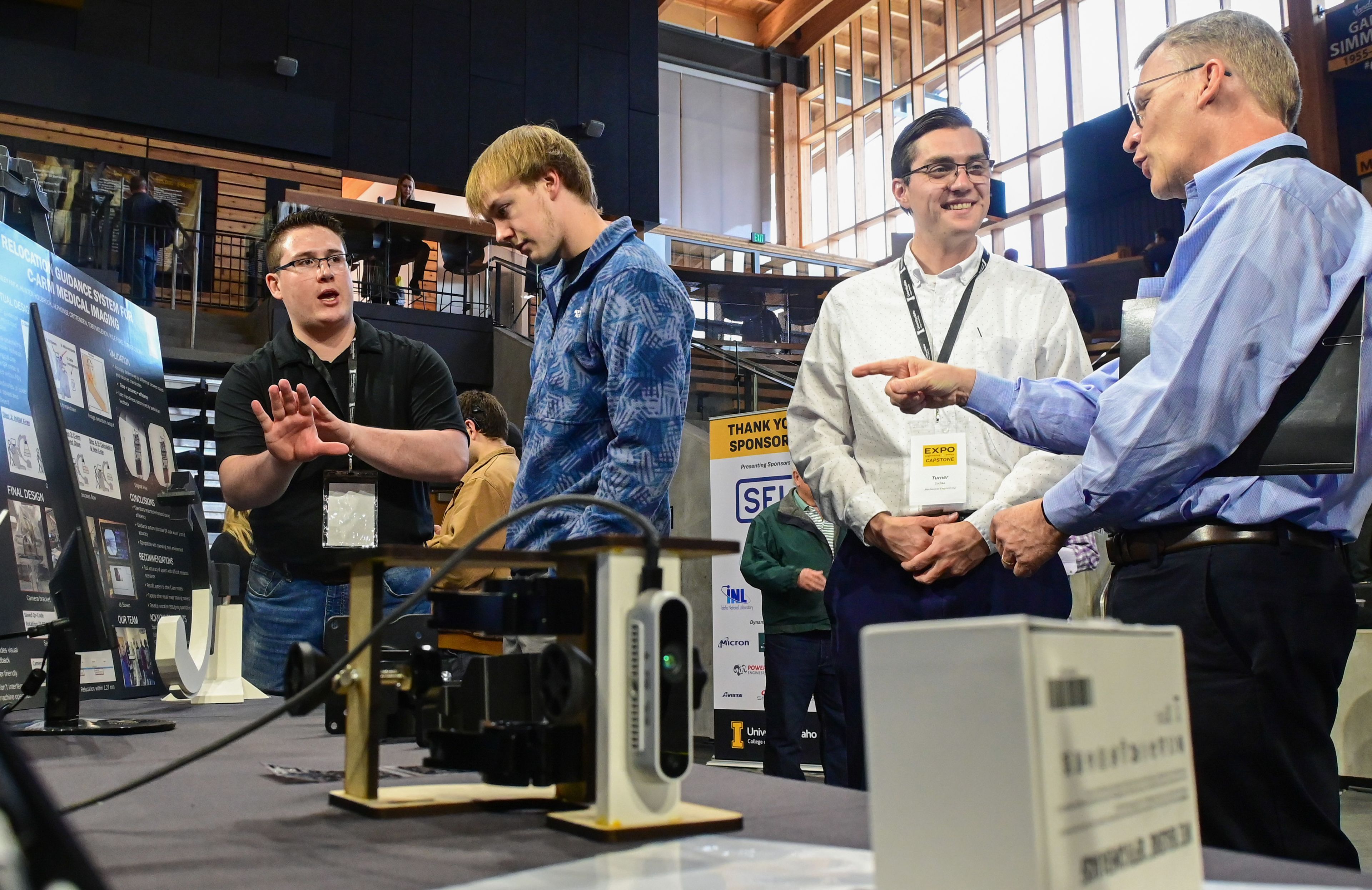 Kyle Fiske, from left, a senior mechanical engineering student at the University of Idaho, talks with project mentor and graduate student Keenan Bryan, while teammate and fellow senior mechanical engineering student Turner Zischka speaks with EXPO judge Ron Stubbers about a relocation guidance system created for a C-Arm medical imaging machine at the Engineering Design EXPO capstone presentations in Moscow on Friday.