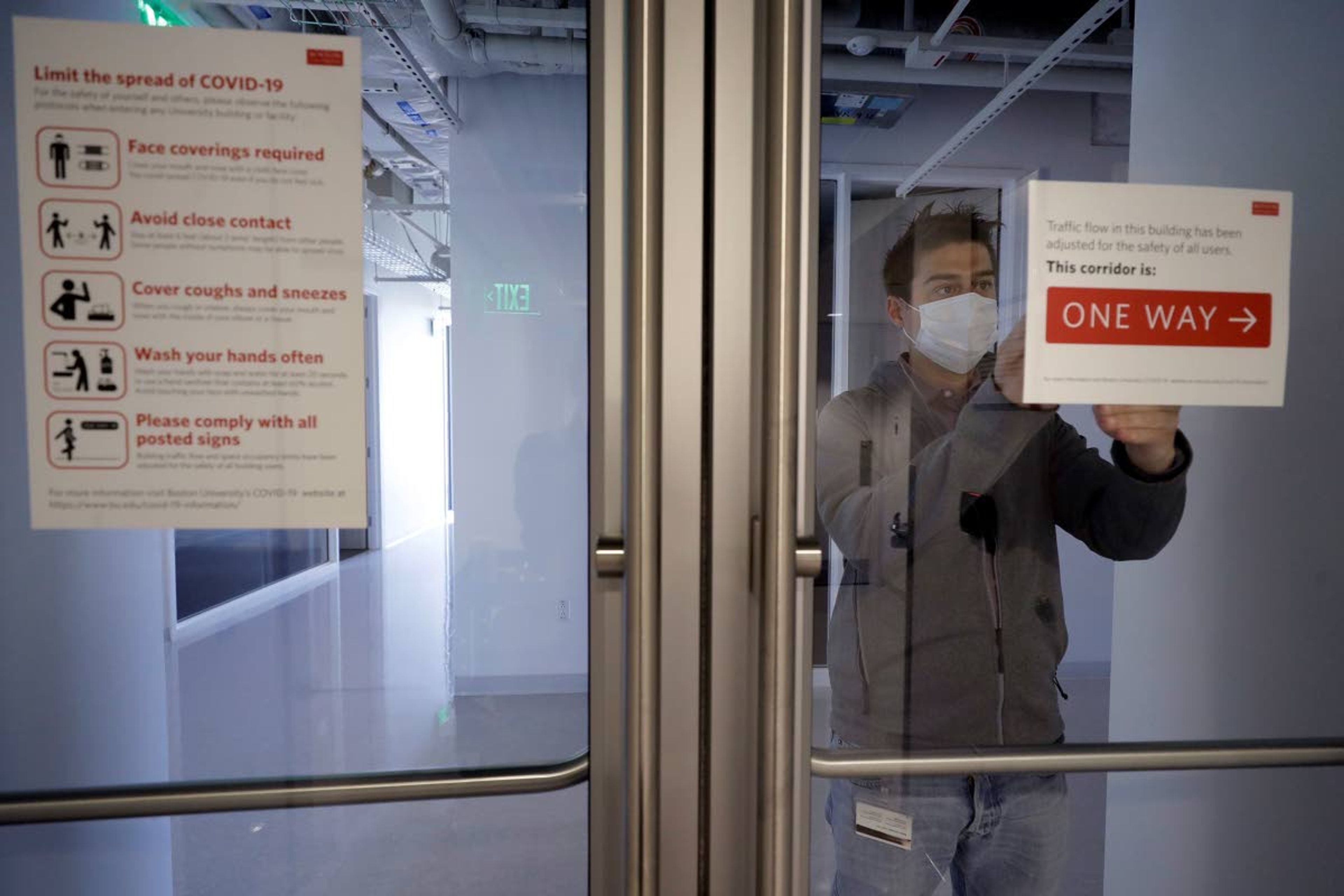 Kevin Gonzales, director of operations at the Rajen Kilachand Center for Integrated Life Sciences and Engineering, at Boston University, places safe distancing signage on glass doors on the school's campus, in Boston, Thursday, May 21, 2020. Boston University is among a growing number of universities making plans to bring students back to campus this fall, but with new measures meant to keep the coronavirus at bay. (AP Photo/Steven Senne)