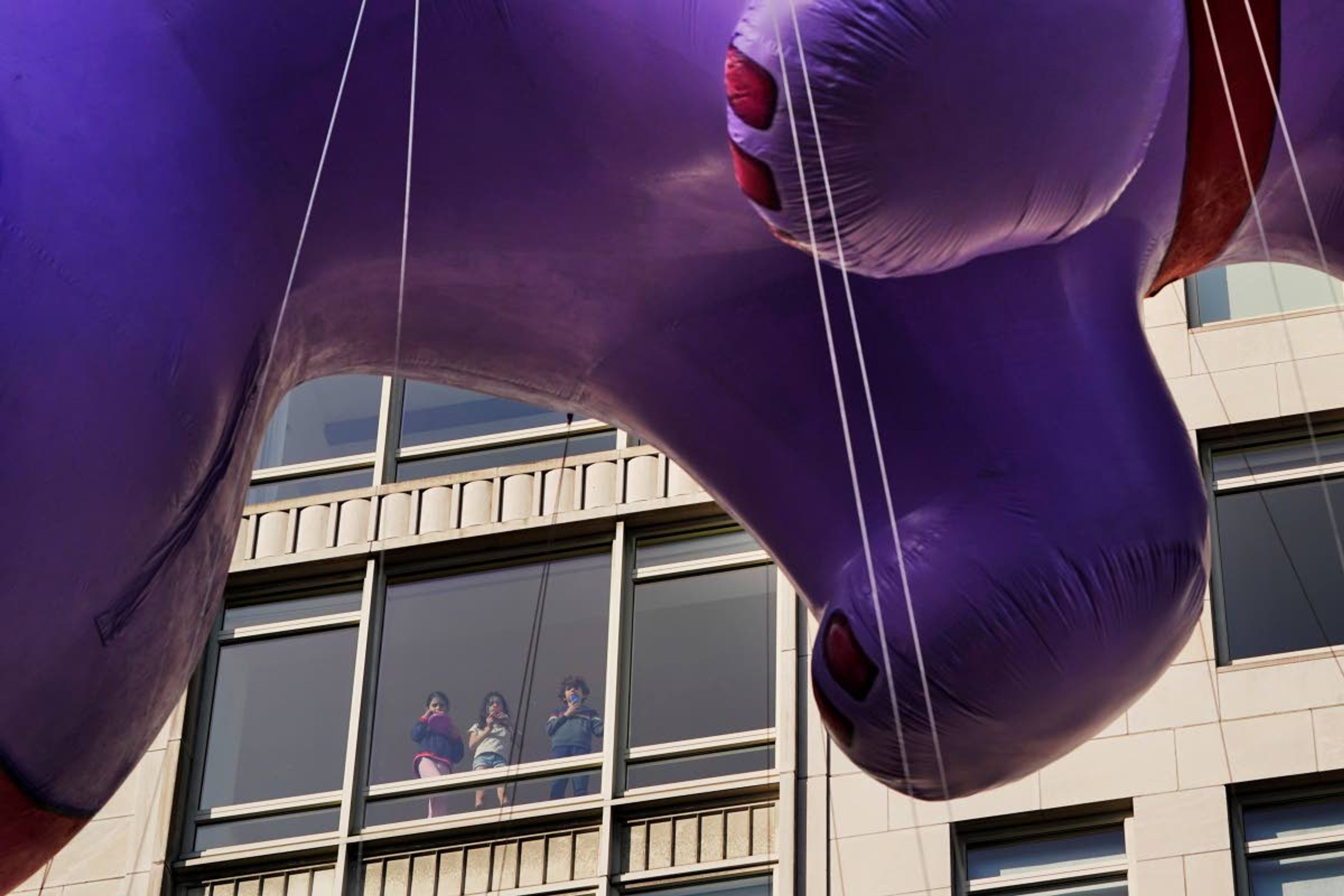 Youngsters watch from a window as balloons from the Macy's Thanksgiving Day Parade pass by, Thursday, Nov. 25, 2021, in New York. The parade is returning in full, after being crimped by the coronavirus pandemic last year. (AP Photo/Seth Wenig)