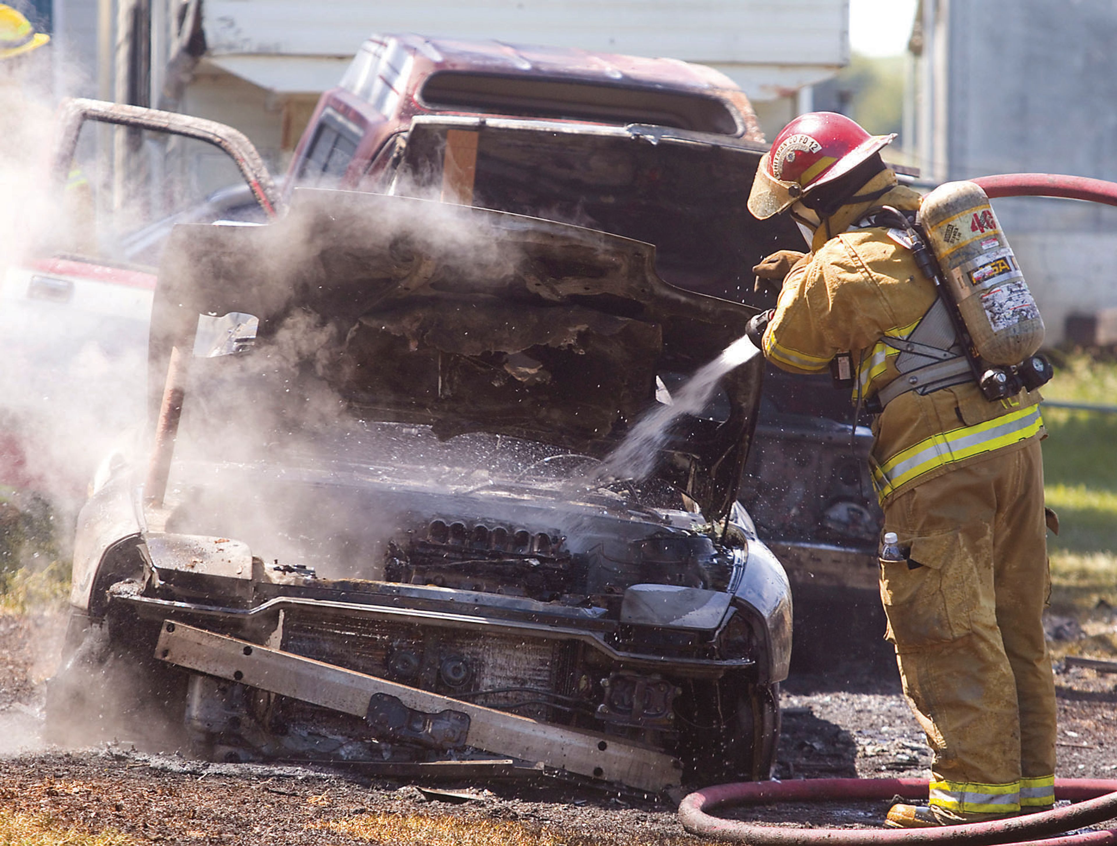 A firefighter extinguishes one of the two cars that burned along with a motorhome outside a home in Palouse.