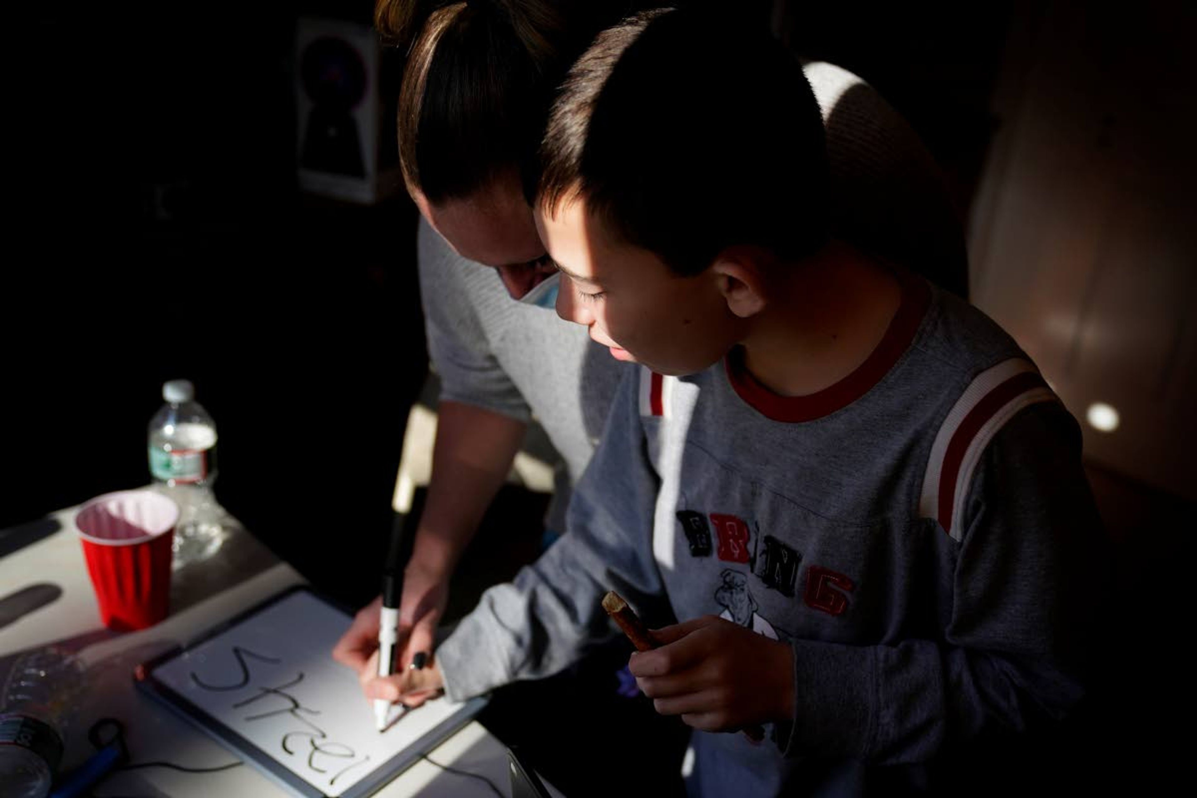 Paraprofessional Jessica Wein helps Josh Nazzaro write numbers while attending class virtually from his home in Wharton, N.J., Wednesday, Nov. 18, 2020. The pandemic is threatening to wipe out the educational progress made by many of the nation’s 7 million students with disabilities. That's according to advocates, who say the extended months of learning from home and erratic attempts to reopen schools are deepening a crisis that began with the switch to distance learning in March. (AP Photo/Seth Wenig)