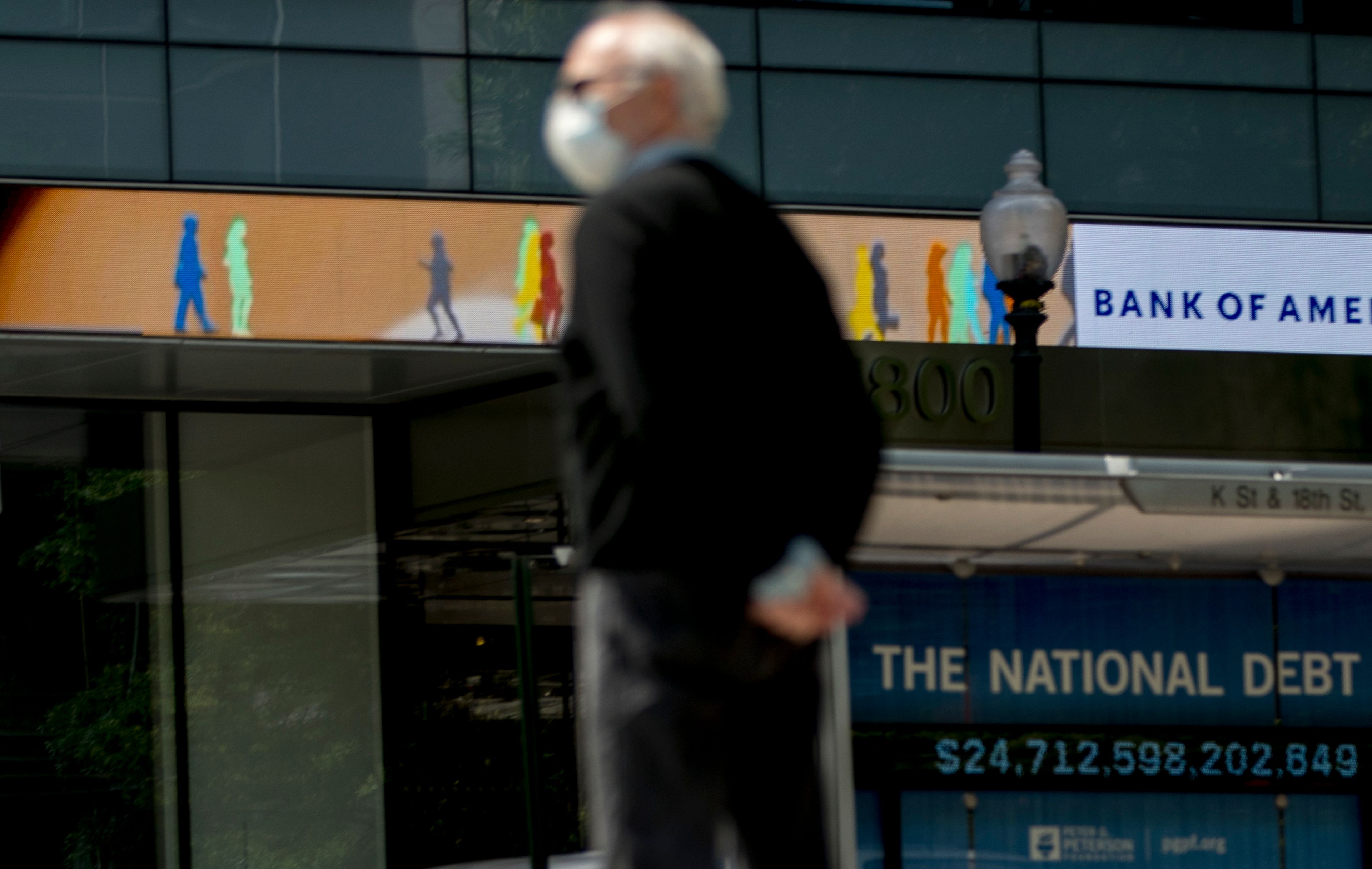 FILE - In this April 29, 2020 file photo, a man wearing a mask to protect against coronavirus, waits to cross the street as a digital sign displays groups of people walking above another sign displaying the size of the national debt along an empty K Street in Washington. The U.S. budget deficit hit an all-time high of $3 trillion for the first 11 months of this budget year, the Treasury Department said Friday, Sept. 11. (AP Photo/Andrew Harnik, File)