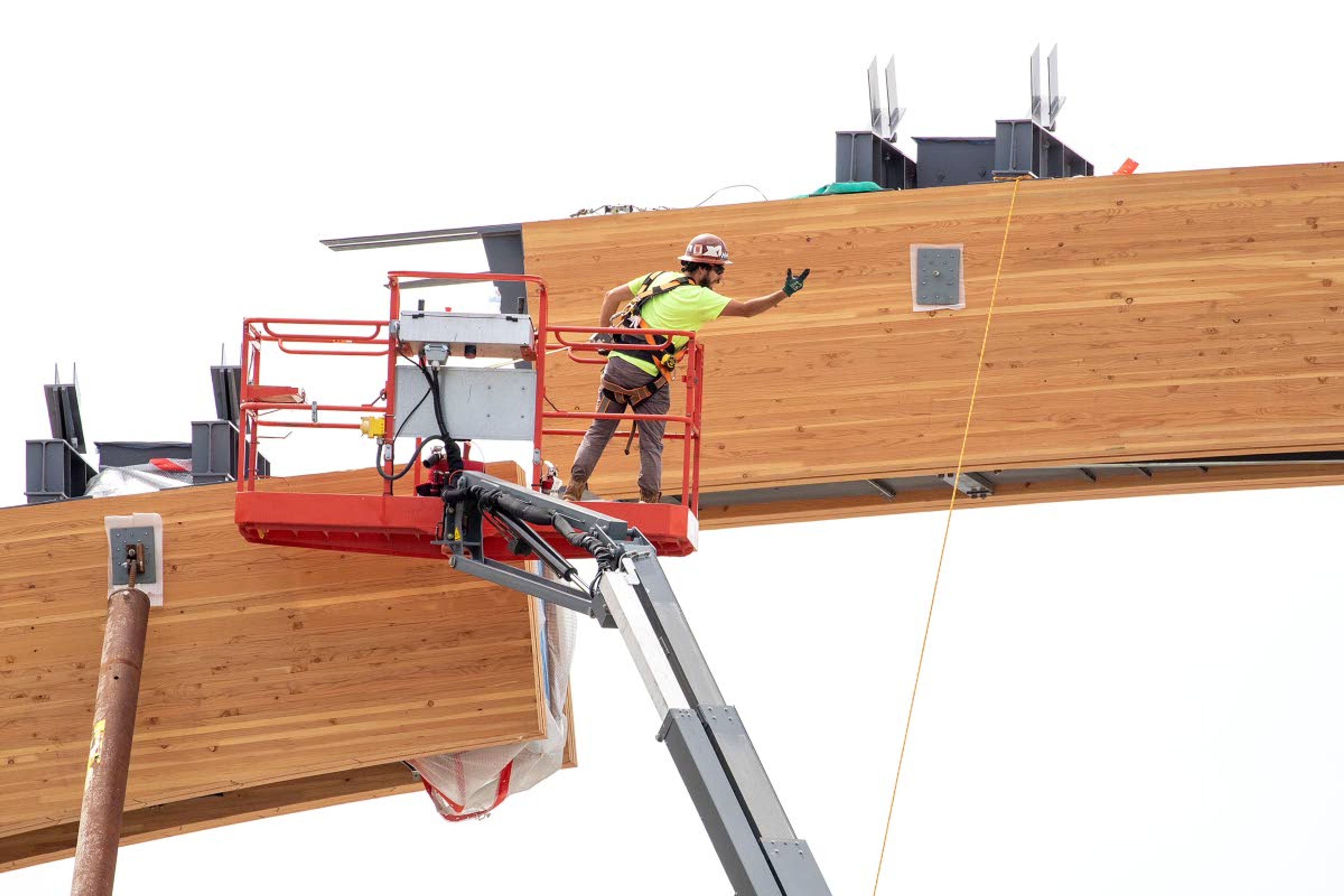 A worker helps guide a laminated wood beam as it is lifted into place with a crane.