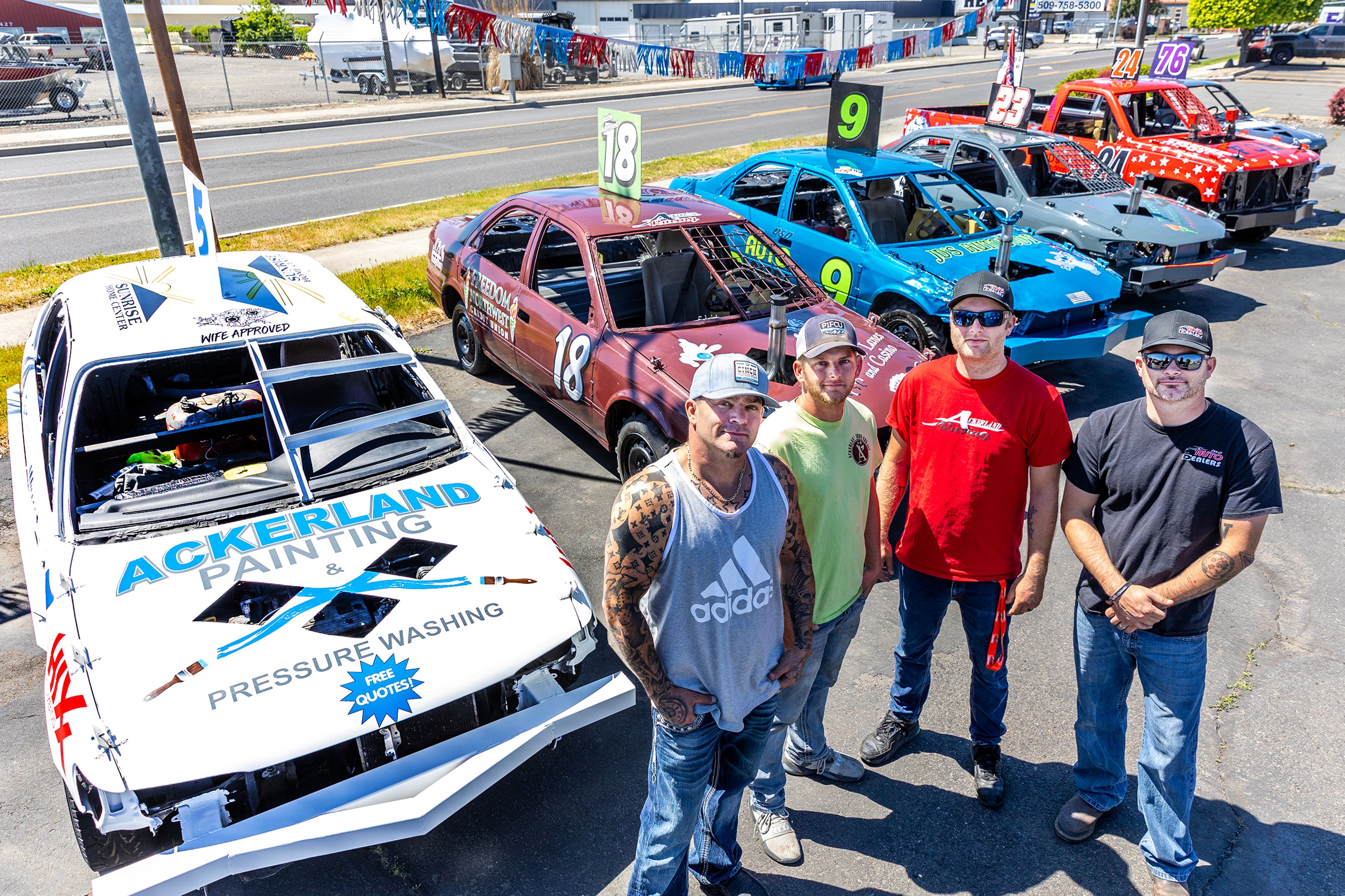 Michael Johns, from left, who drives car No. 23 and 24, Justin Ackerland, driving car No. 18, Dan Ackerland, driving car No. 9, and David Ackerland, driving car No. 76, stand in front of derby cars at Discount Auto Sales Thursday in Clarkston.