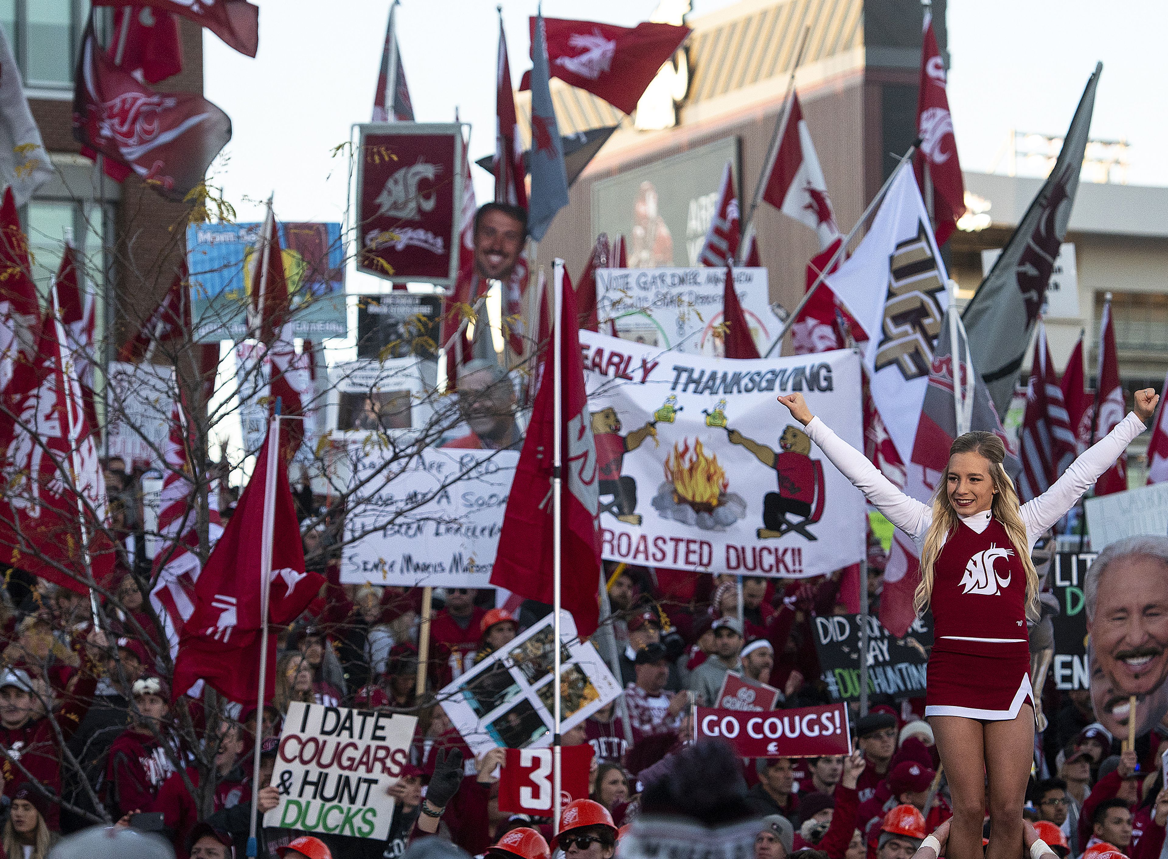 Washington State flags and hand-made signs are waved in the background as the Cougar Cheer Squad performs behind the College GameDay stage on Saturday morning in Pullman.