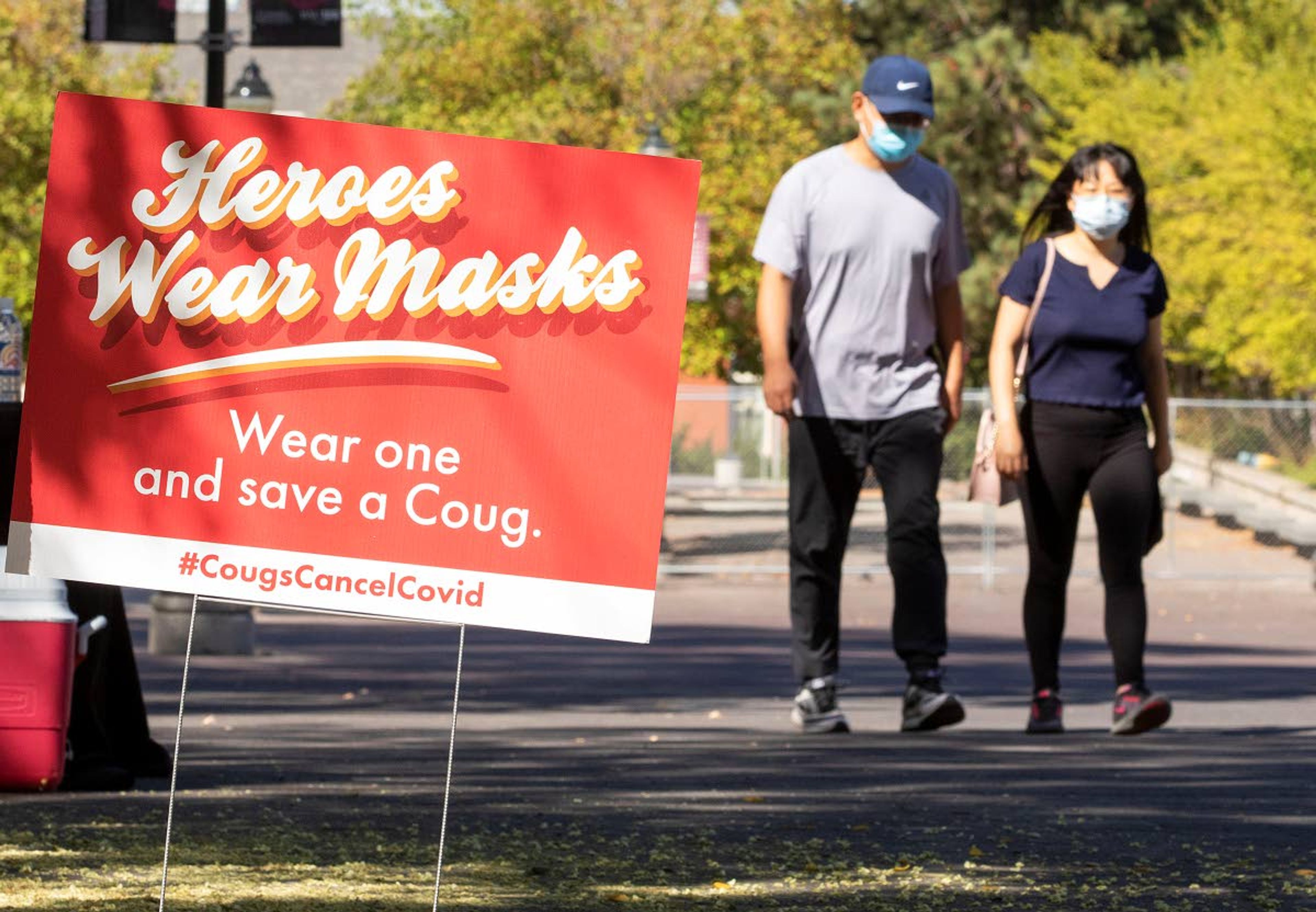 Pedestrians walk by a sign outside the Compton Union Building reminding students to wear a mask Friday at Washington State University in Pullman. The University has launched the Cougs Cancel COVID campaign after a surge in the number of students testing positive for COVID-19 this week.