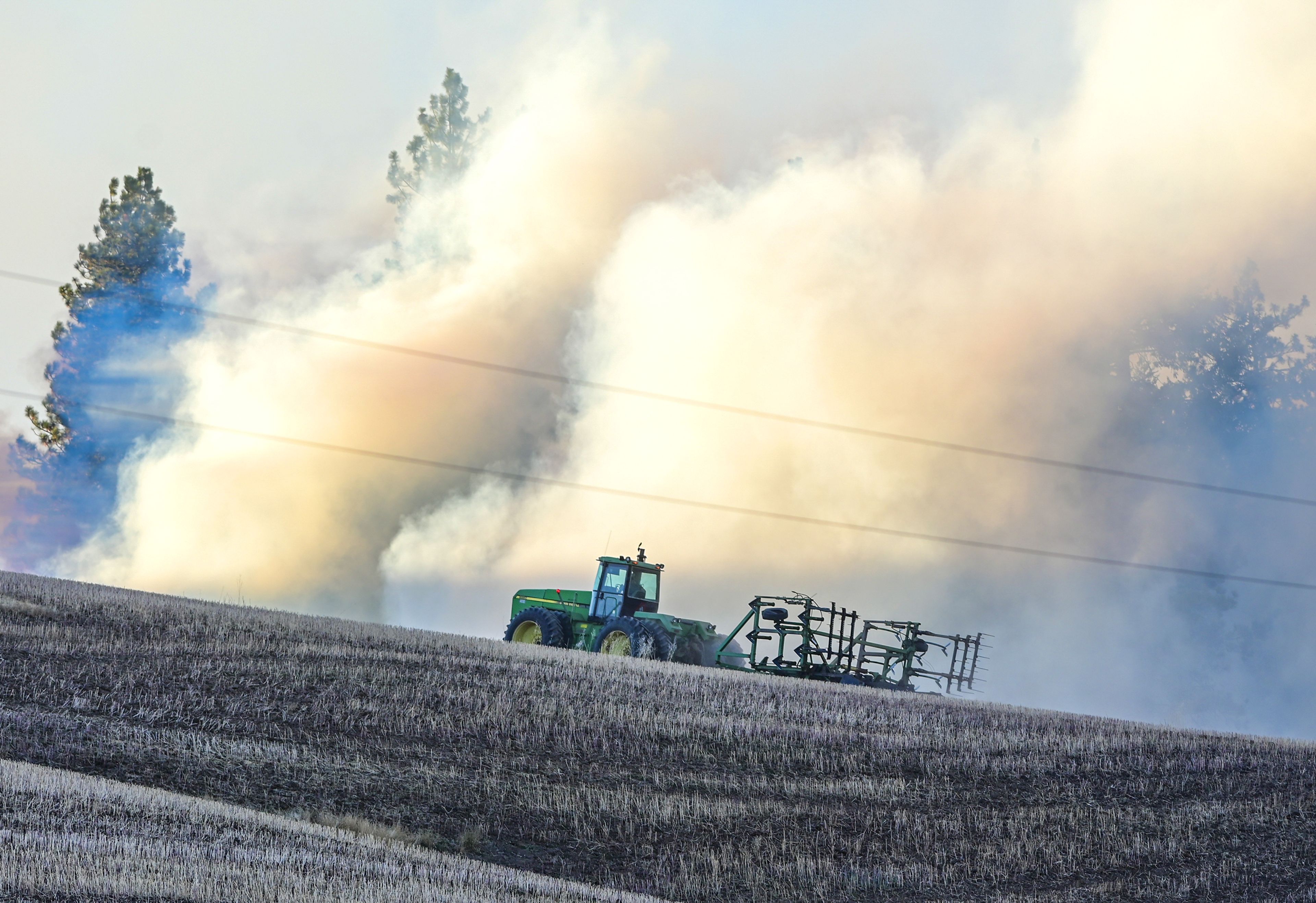 A tractor moves up a hill along Teare Road toward smoke rising from a wildfire Friday in Moscow.,