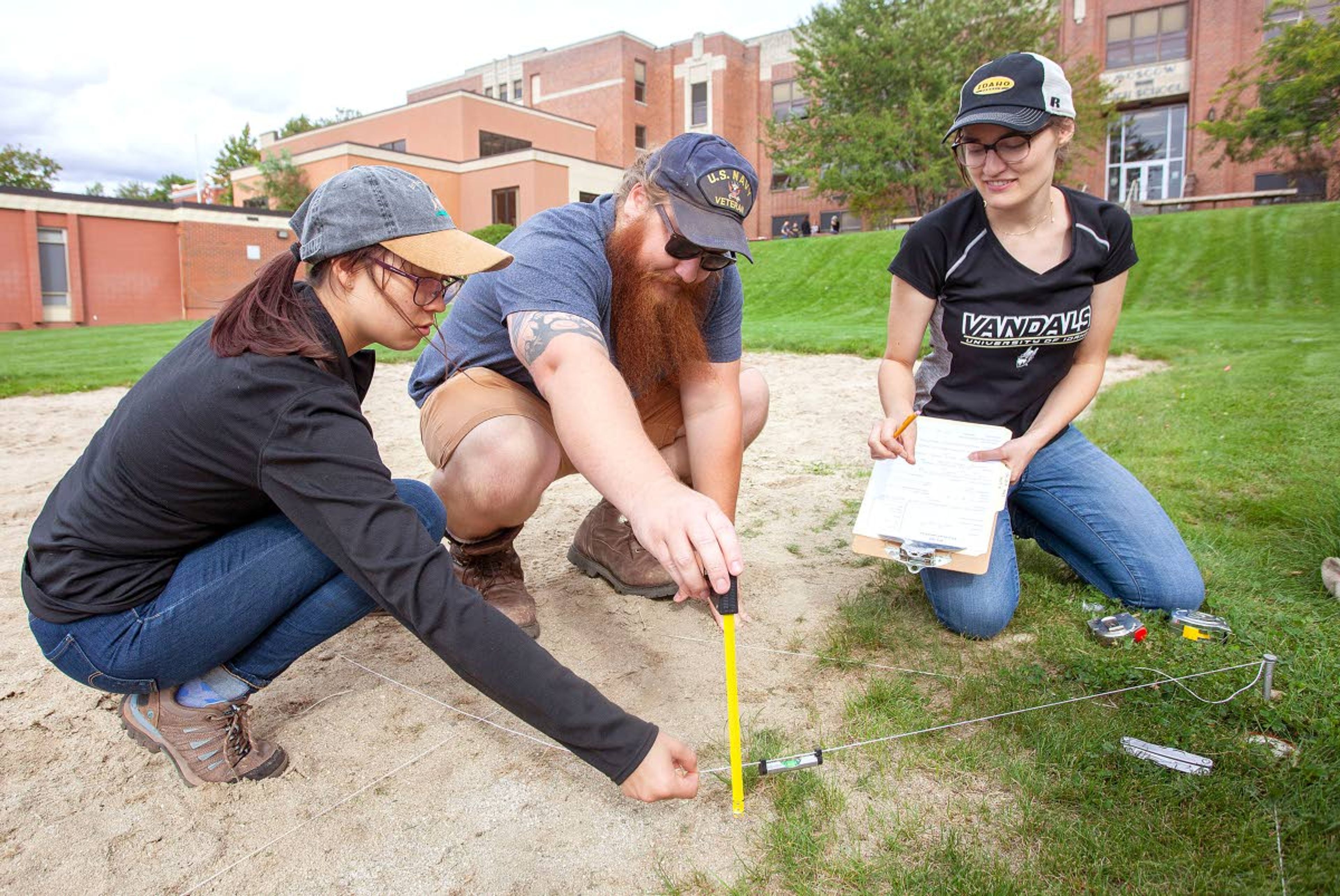 University of Idaho anthropology students Willow Elsom (left to right), John Bergner and Tessie Burningham set up an excavation unit at an archeological site Friday outside Moscow High School.