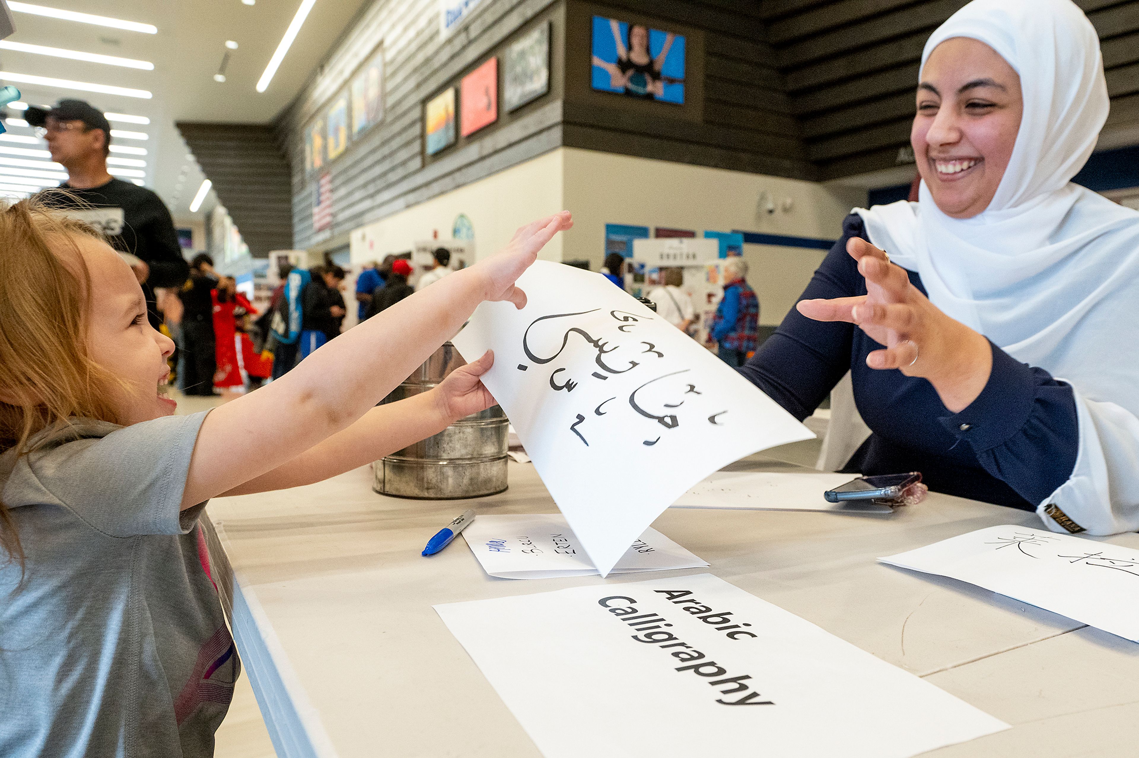 Washington State University student Laila Bensaud hands over a piece of paper to Maysie Montoya with Maysie’s name written in Arabic calligraphy Friday at Pullman High School’s multicultural night.