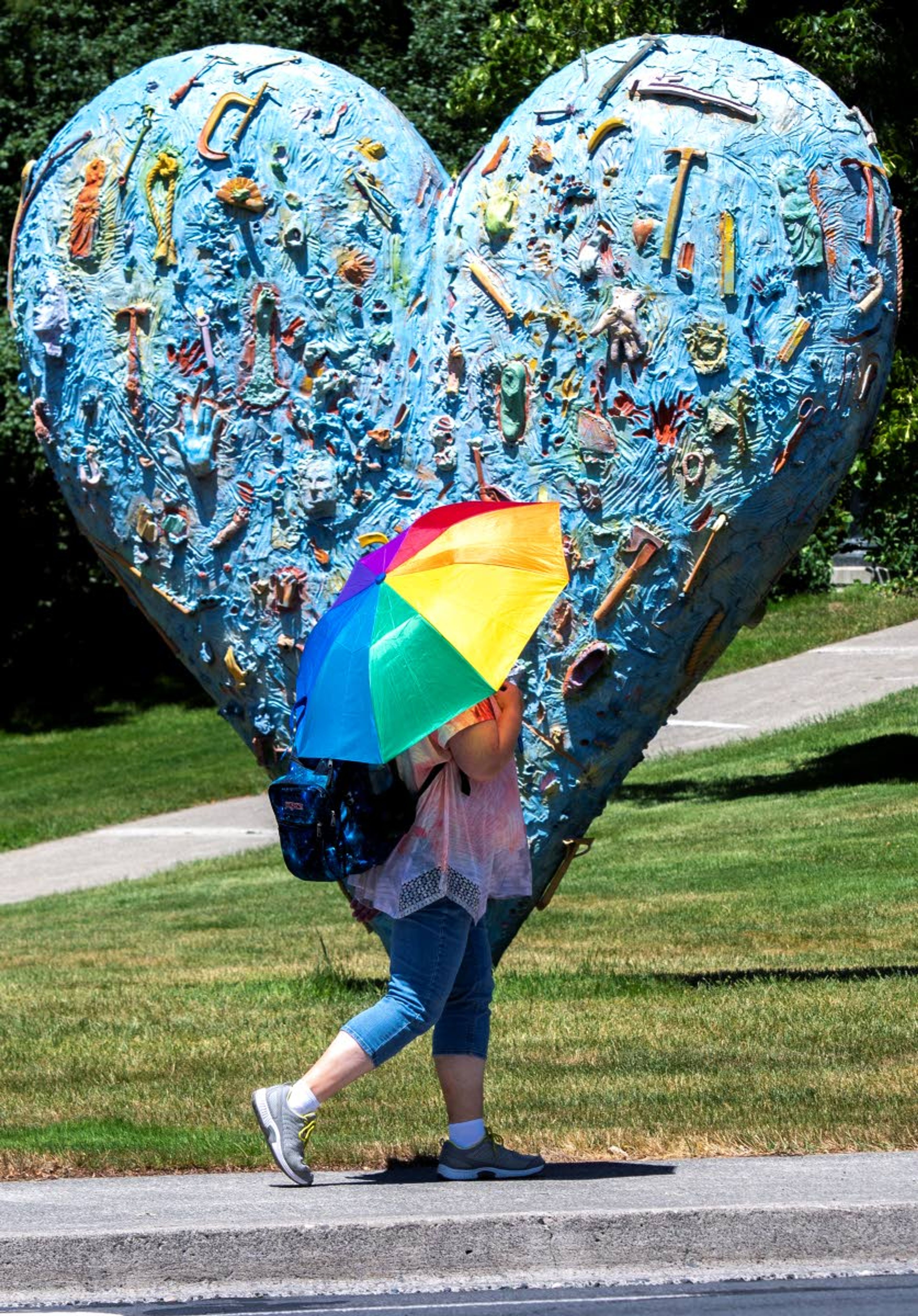 A pedestrian tries to beat the heat with an umbrella Thursday as she walks in front of “The Technicolor Heart” artwork on the Washington State University campus.