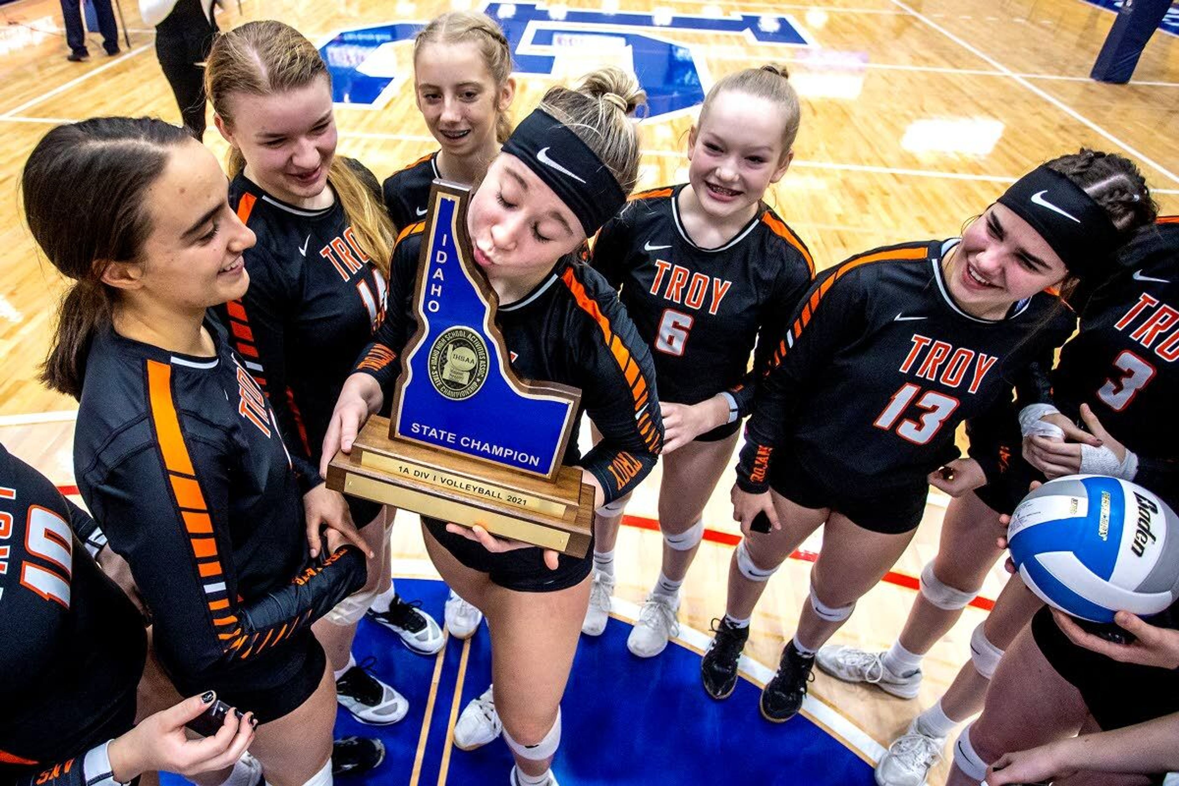 Troy’s Morgan Blazzard kisses the championship trophy as teammates surround her after the Trojans won the Idaho Class 1A Division I state volleyball title Saturday against Grace at the LCSC Activity Center.