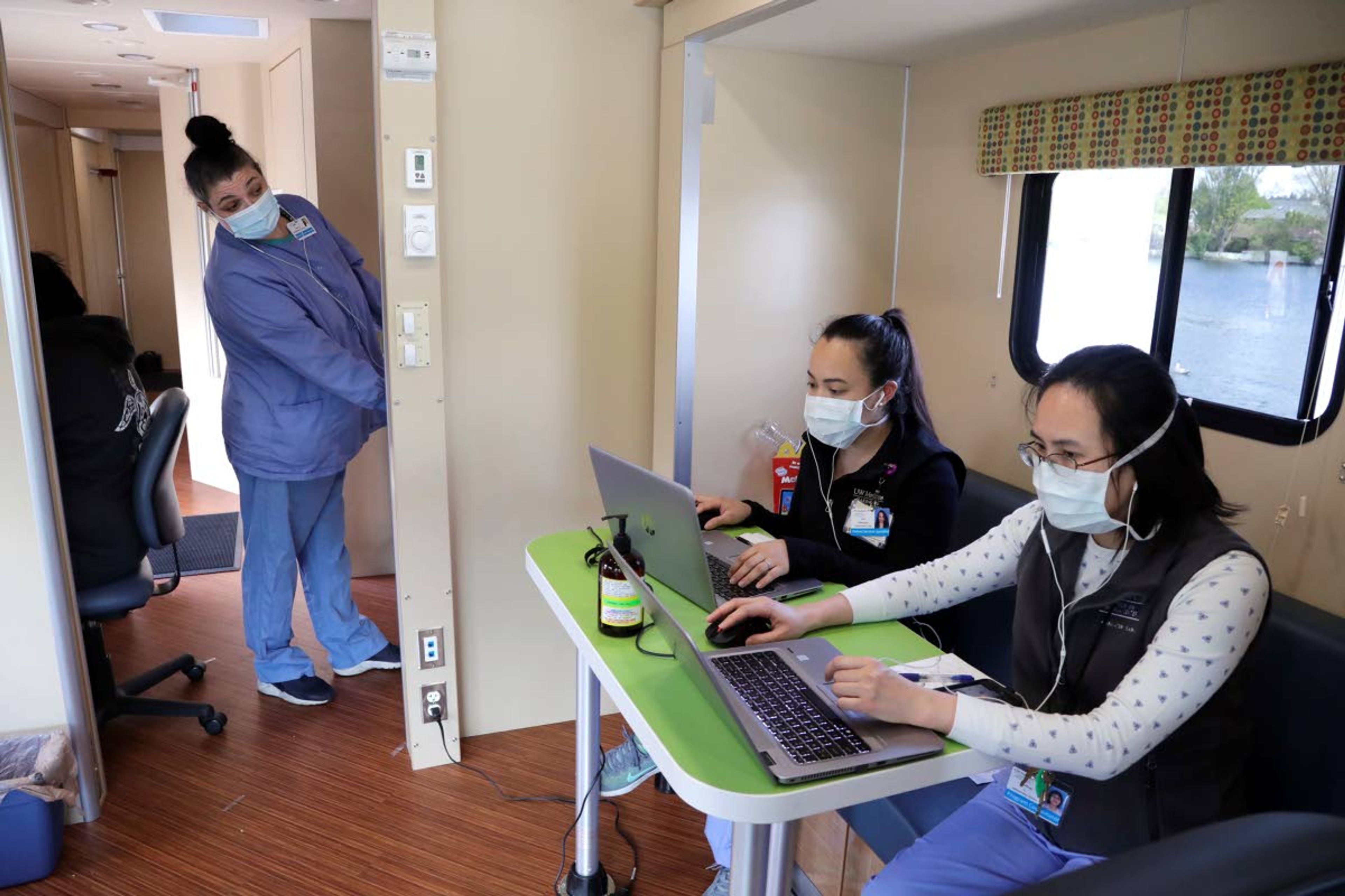 Sarah VanBuskirk, left, looks across to talk with fellow patient service specialists Yuehua Liang, right, and Eva Villanueva as they prepare records via cell phone for patients driving up to a coronavirus testing site Wednesday, April 29, 2020, in Seattle. The site, open Wednesdays and Saturdays from 10 a.m. to 3 p.m. in the Rainier Beach neighborhood, is available to anyone displaying the virus symptoms, are pregnant, over 60 or have a chronic condition, as well as health care workers and first responders. (AP Photo/Elaine Thompson)