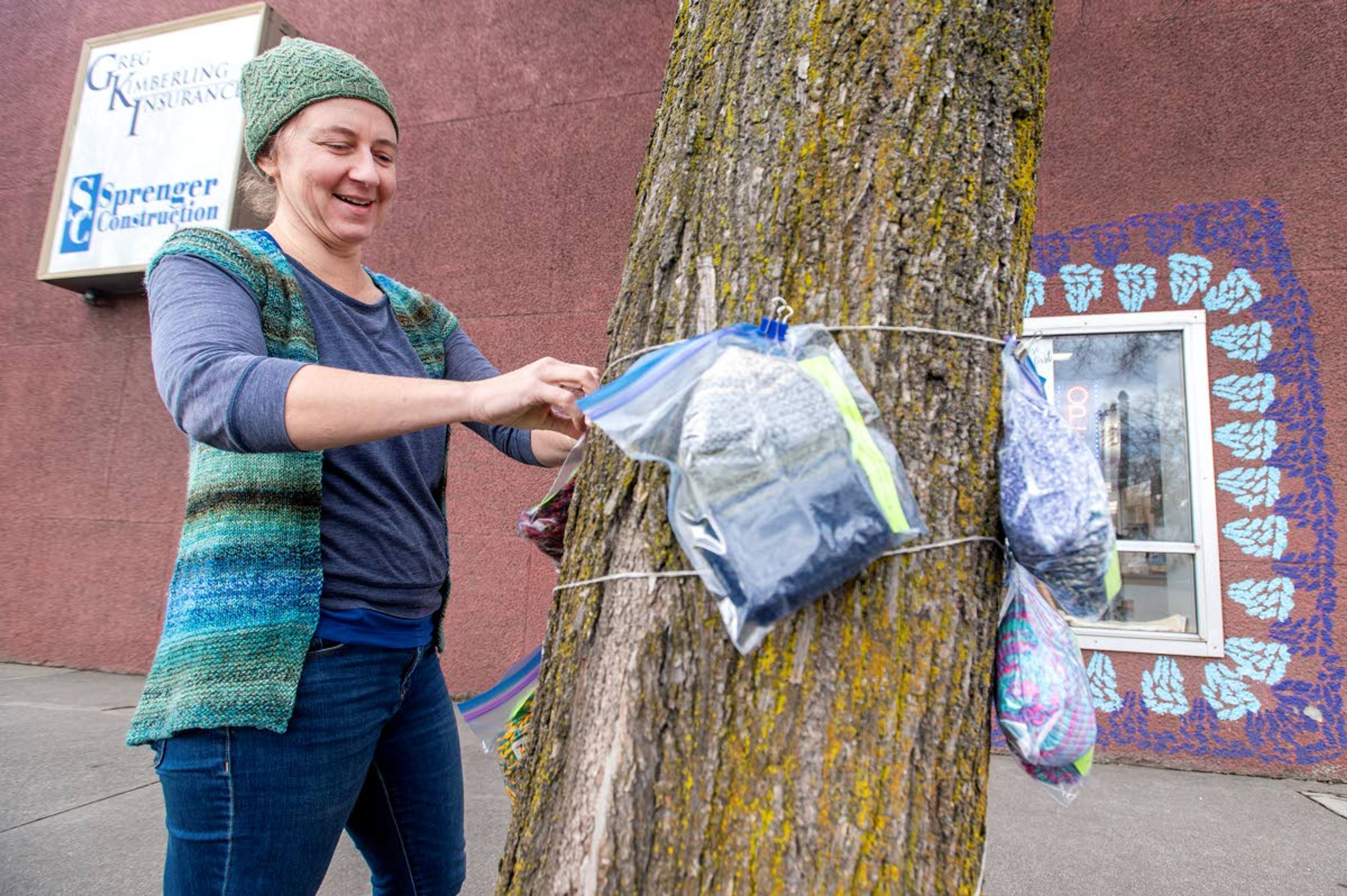 Shelley Stone, owner of The Yarn Underground, hangs ziploc bags containing knitted hats on a tree outside of her store on Wednesday afternoon in downtown Moscow. Stone said that the hats were donated and available to anyone that walks past.