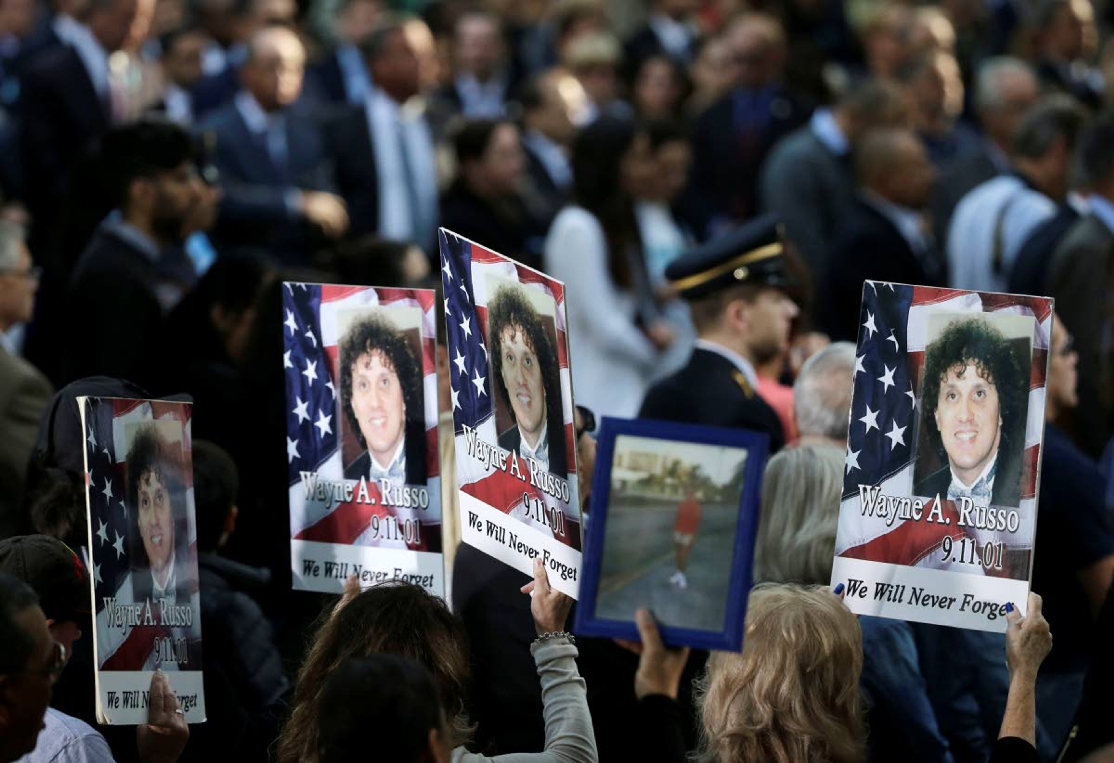 FILE - In this Sept. 11, 2017, file photo, people hold up signs with the names and pictures of victims of the 9/11 terrorist attacks during a ceremony at ground zero in New York. The coronavirus pandemic has reshaped how the U.S. is observing the anniversary of 9/11. The terror attacks' 19th anniversary will be marked Friday, Sept. 11, 2020, by dueling ceremonies at the Sept. 11 memorial plaza and a corner nearby in New York. (AP Photo/Seth Wenig, File)