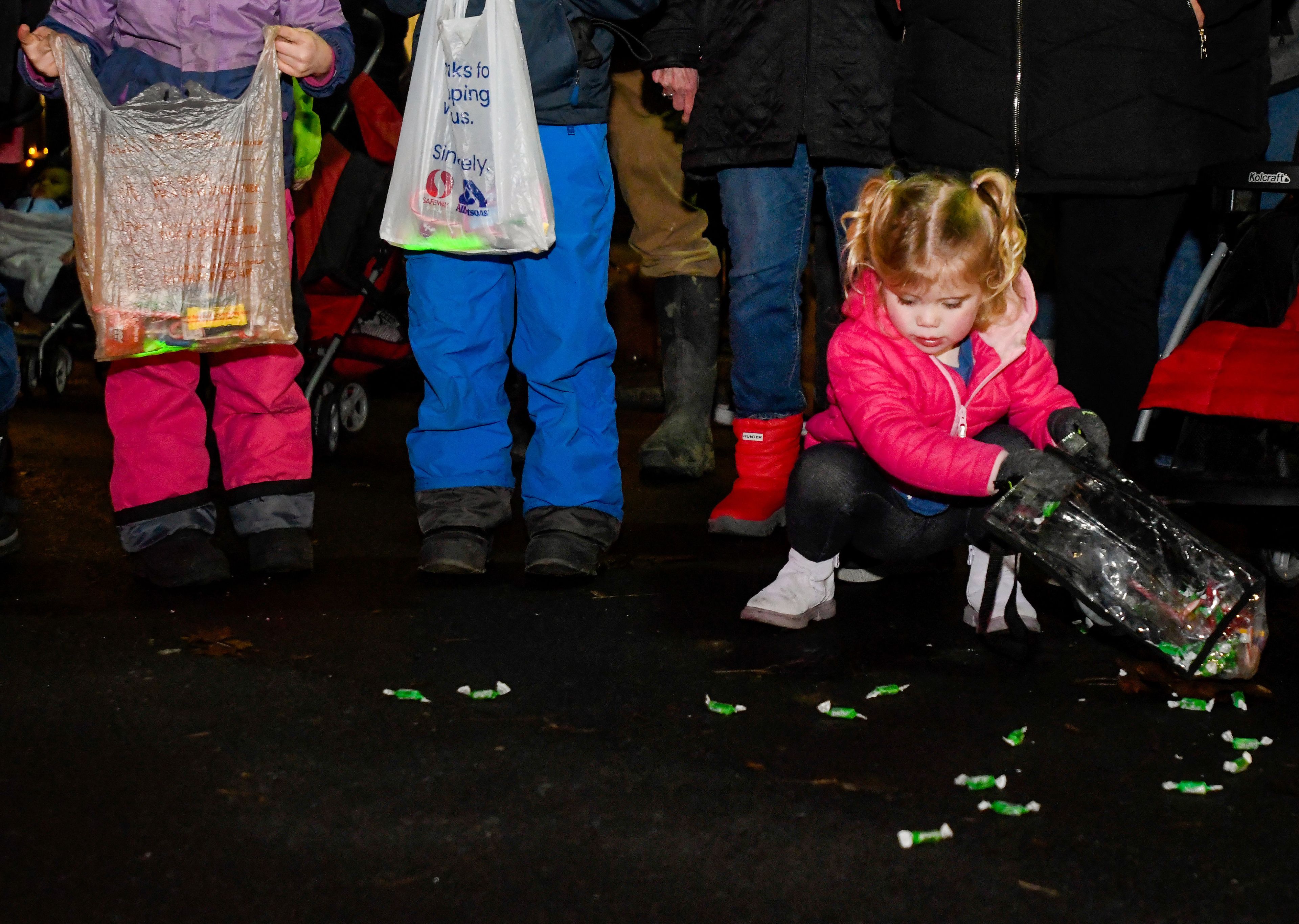 Alice Loiacono, 3, crouches down to collect candy off Main Street from the Light Up the Season parade on Thursday.