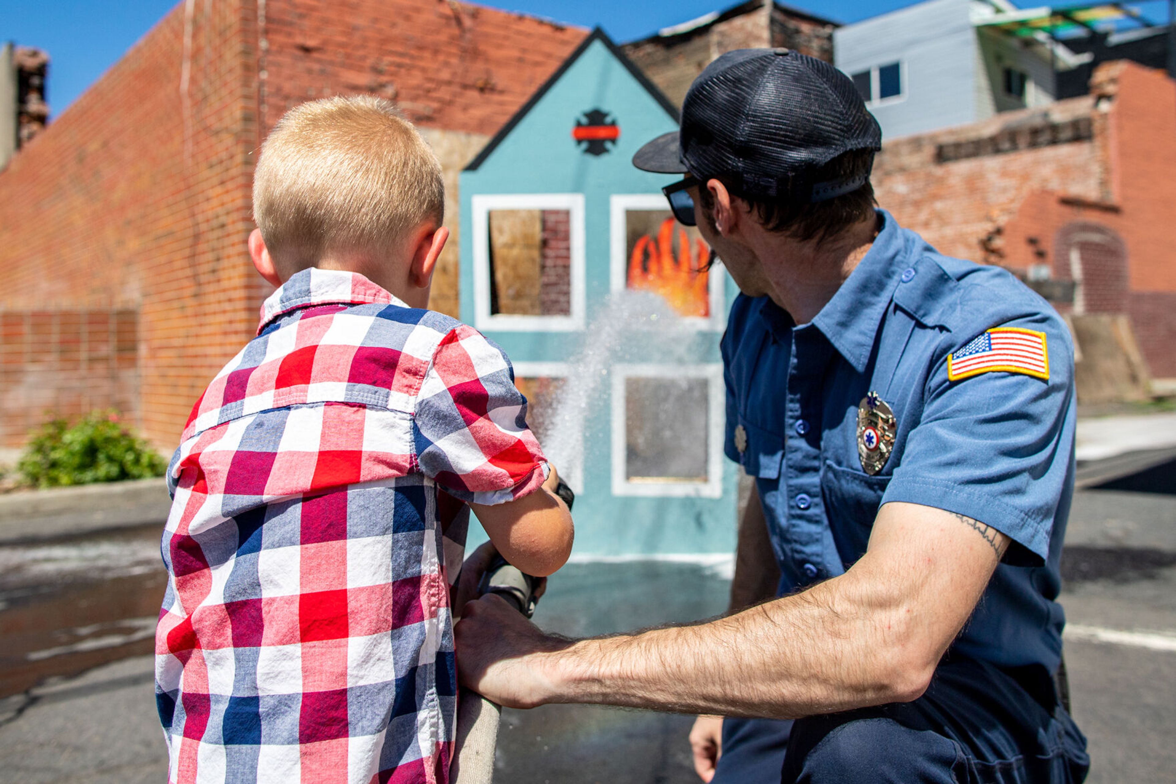 Loyal Abram, 3, of Colfax, practices putting out some mock fires with some help from Colfax fireman John Lautenslager on Saturday during the city of Colfax’s 150th birthday celebration.,