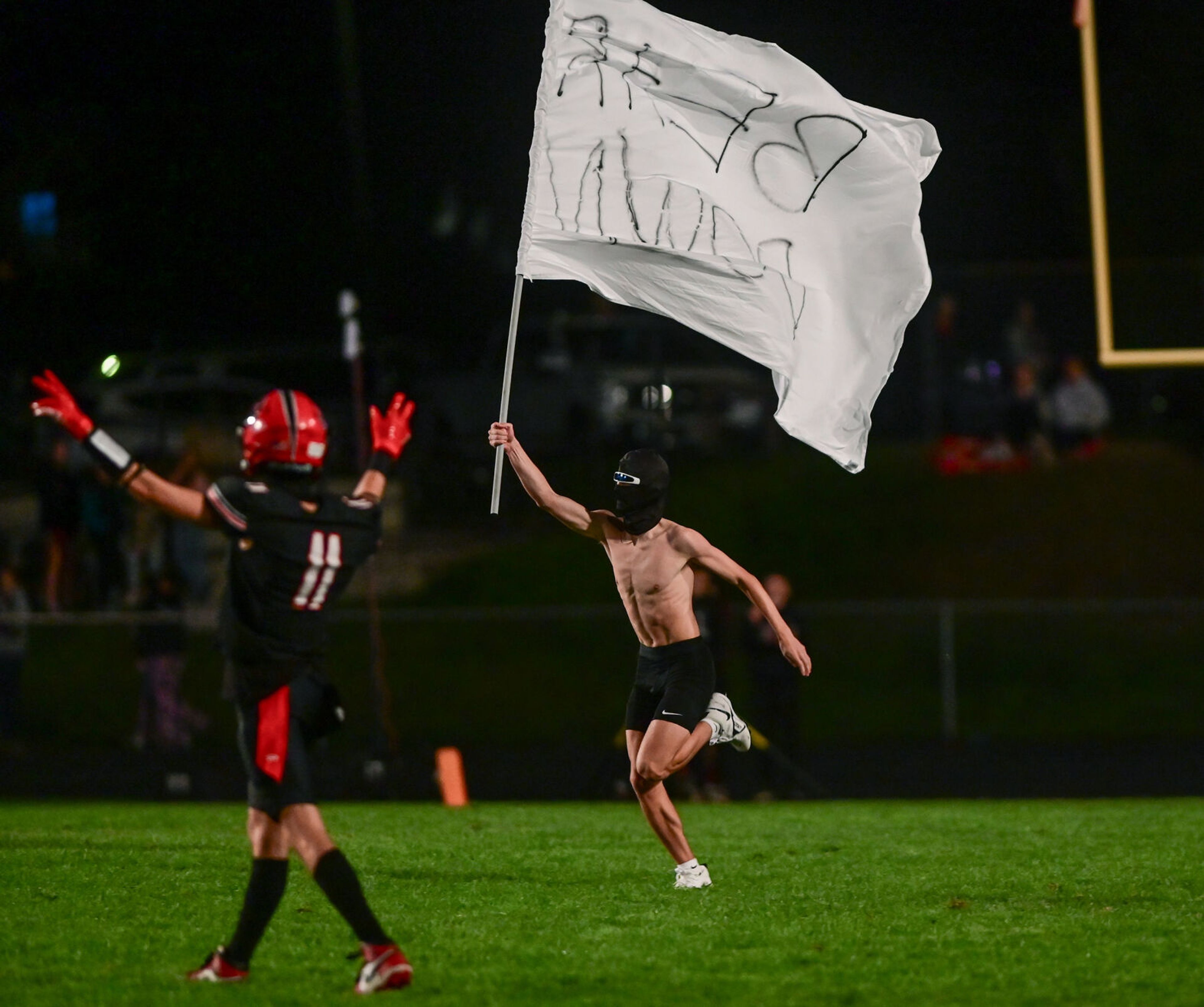 A masked individual runs across the field with a flag that says “Bear Down” as Moscow plays Pullman Friday in Moscow.