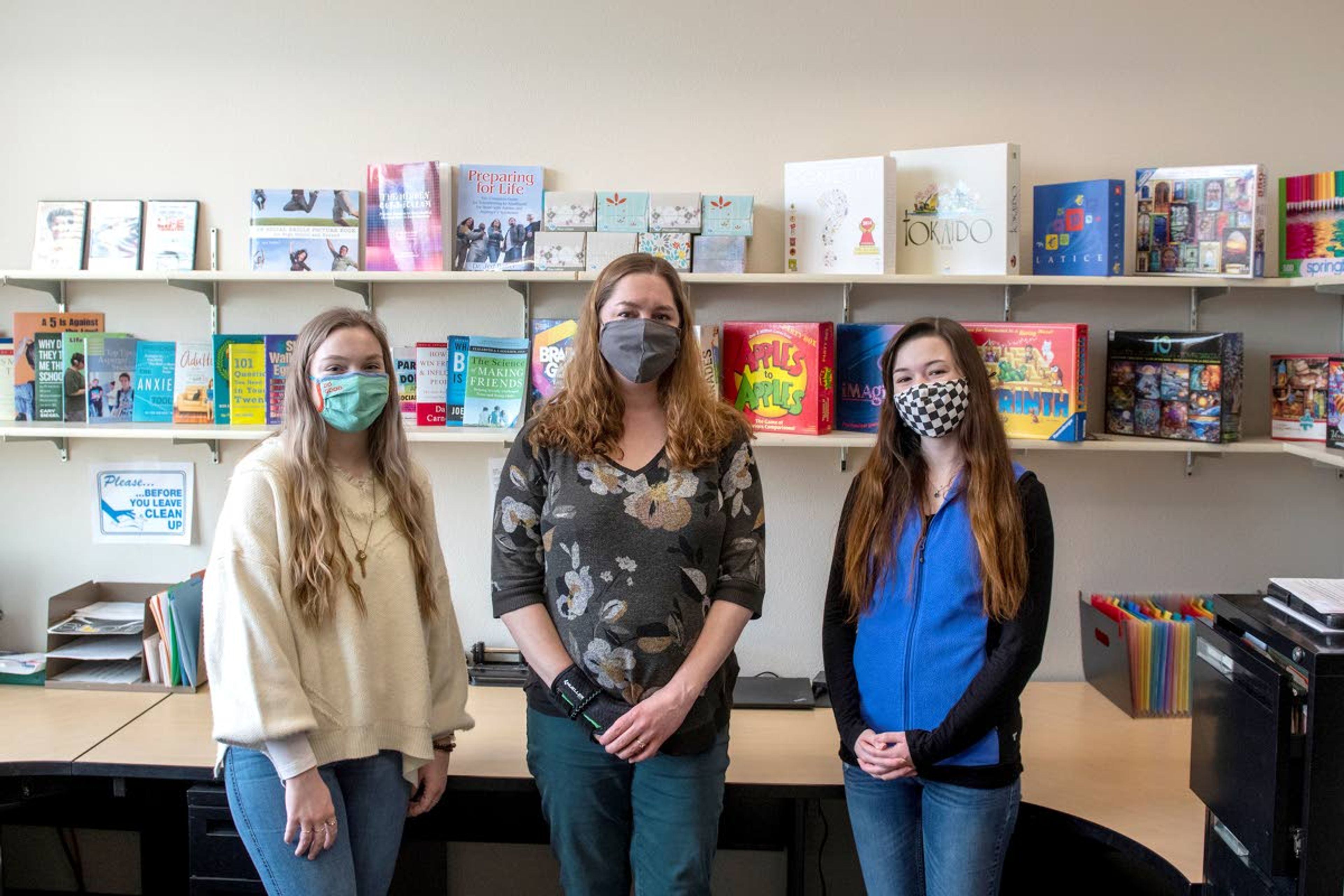 Ravens Scholars Program Coordinator Leslie Gwartney, center, poses Tuesday in front of a collection of books, games and puzzles with work study students Dylanie Frazier, left, and Lyssa Bivens, right, in the Raven Room in the Idaho Student Union Building.