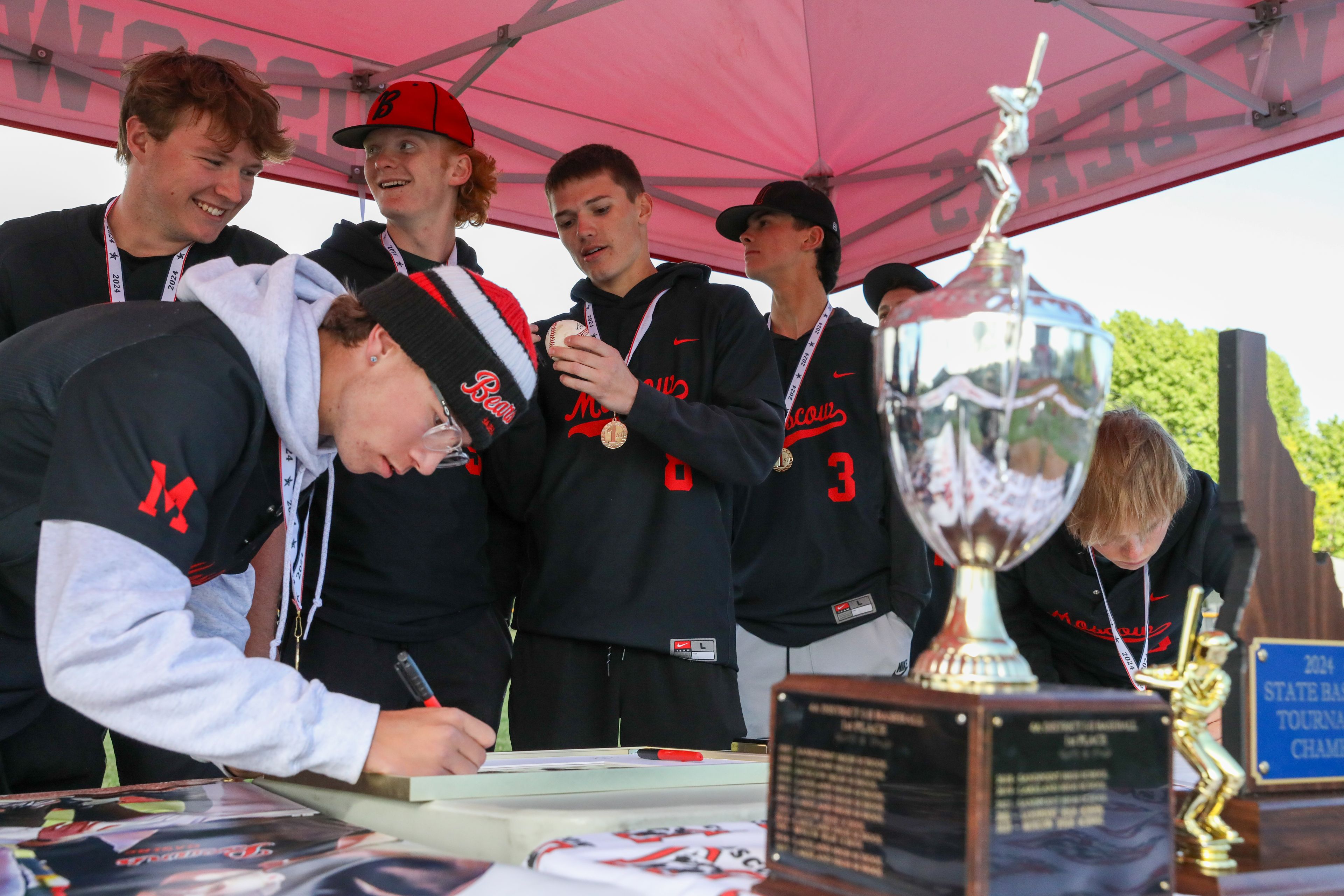 Moscow players sign banners, photos and a game ball from behind their trophies from their state championship run in Moscow on Thursday.