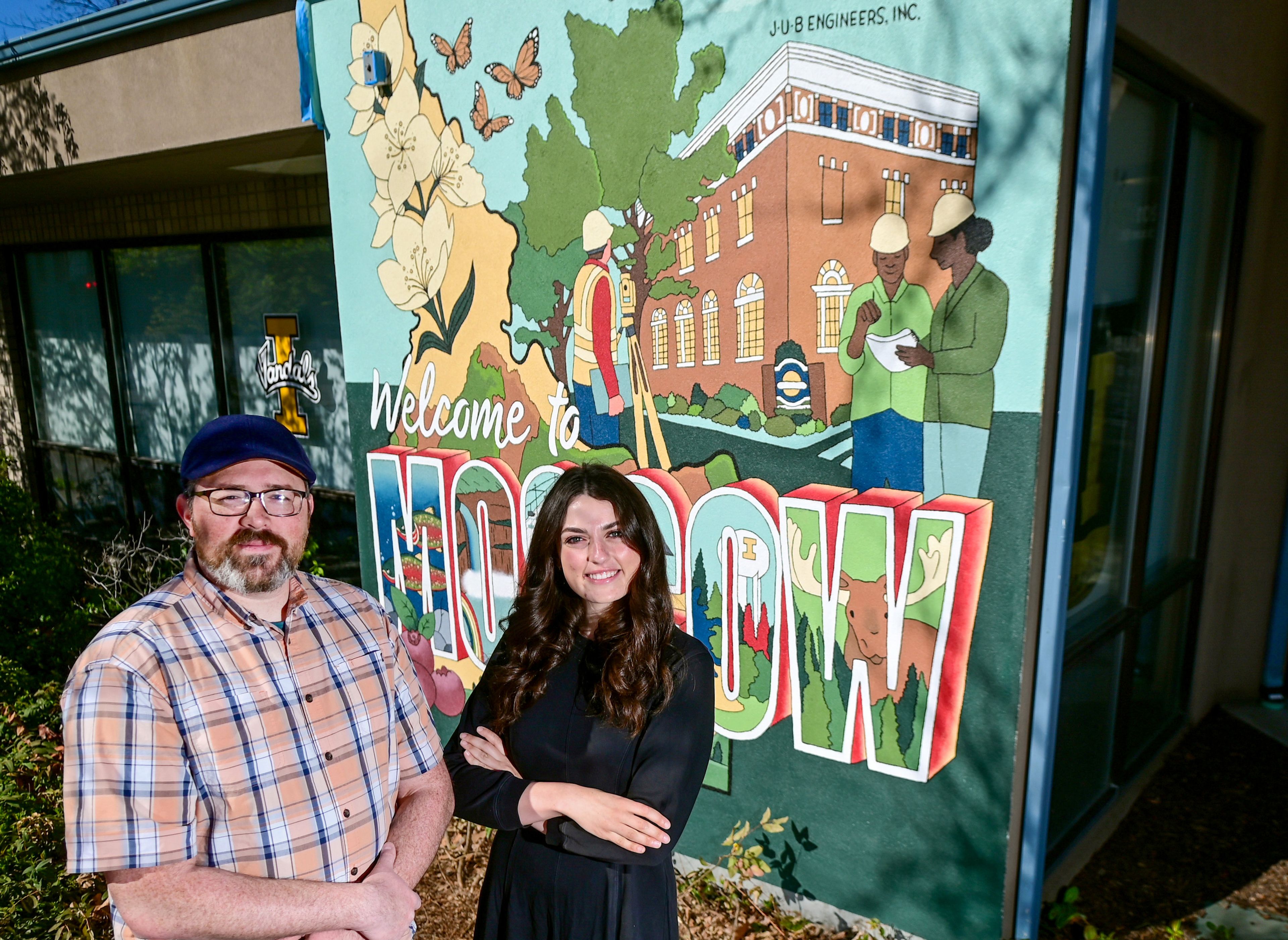 David Watkins, left, Moscow Area Manager with J-U-B Engineers, and Madelynn Gregoire, a University of Idaho graduate student, stand next to a Moscow-themed mural painted by Gregoire on the side of the J-U-B Engineers building in downtown Moscow on Monday.