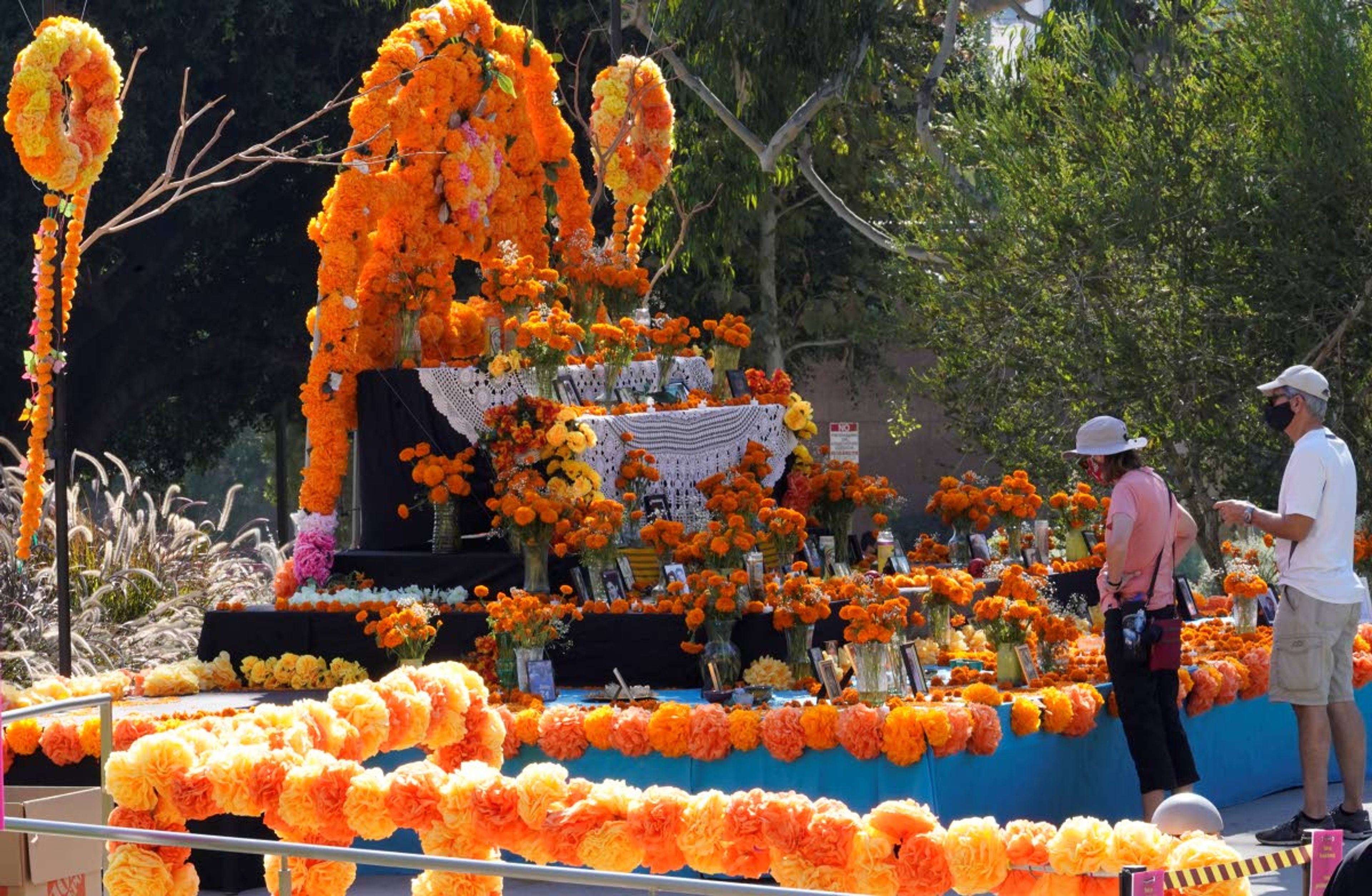 People look at a community altar decorated with marigolds, sometimes called "flowers of the dead," at Grand Park in Los Angeles, Thursday, Oct. 29, 2020. Mother and daughter Chicana artists Ofelia and Rosanna Esparza have overseen the design of the altar at Grand Park since 2013. It's one of 11 huge altars done in a collaboration between Grand Park and Self Help Graphics, an organization highlighting Chicano and Latino artists and social justice. (AP Photo/Damian Dovarganes)