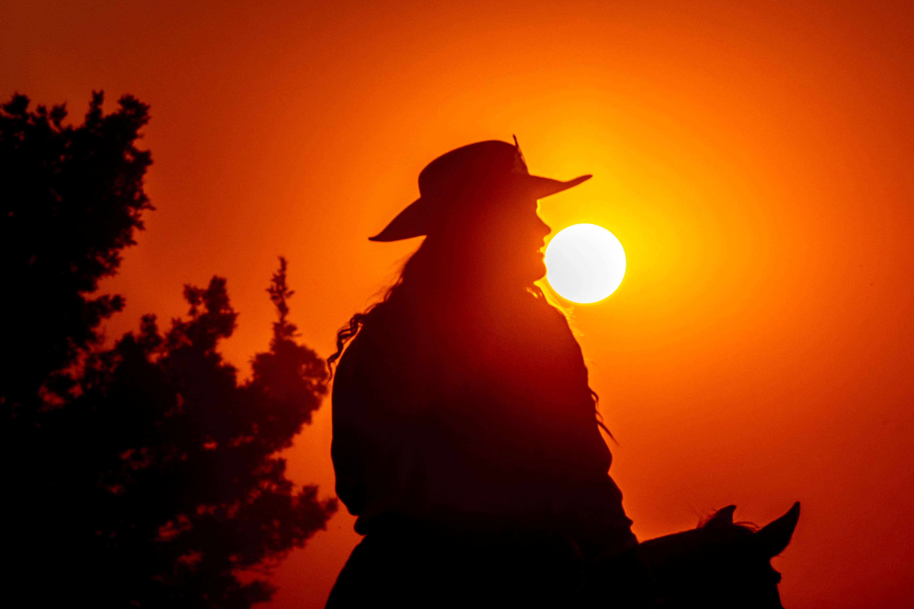 The sun sets as an orb in the sky under hazy conditioners as a cowgirl rides around a side arena on day 3 of the Lewiston Roundup.